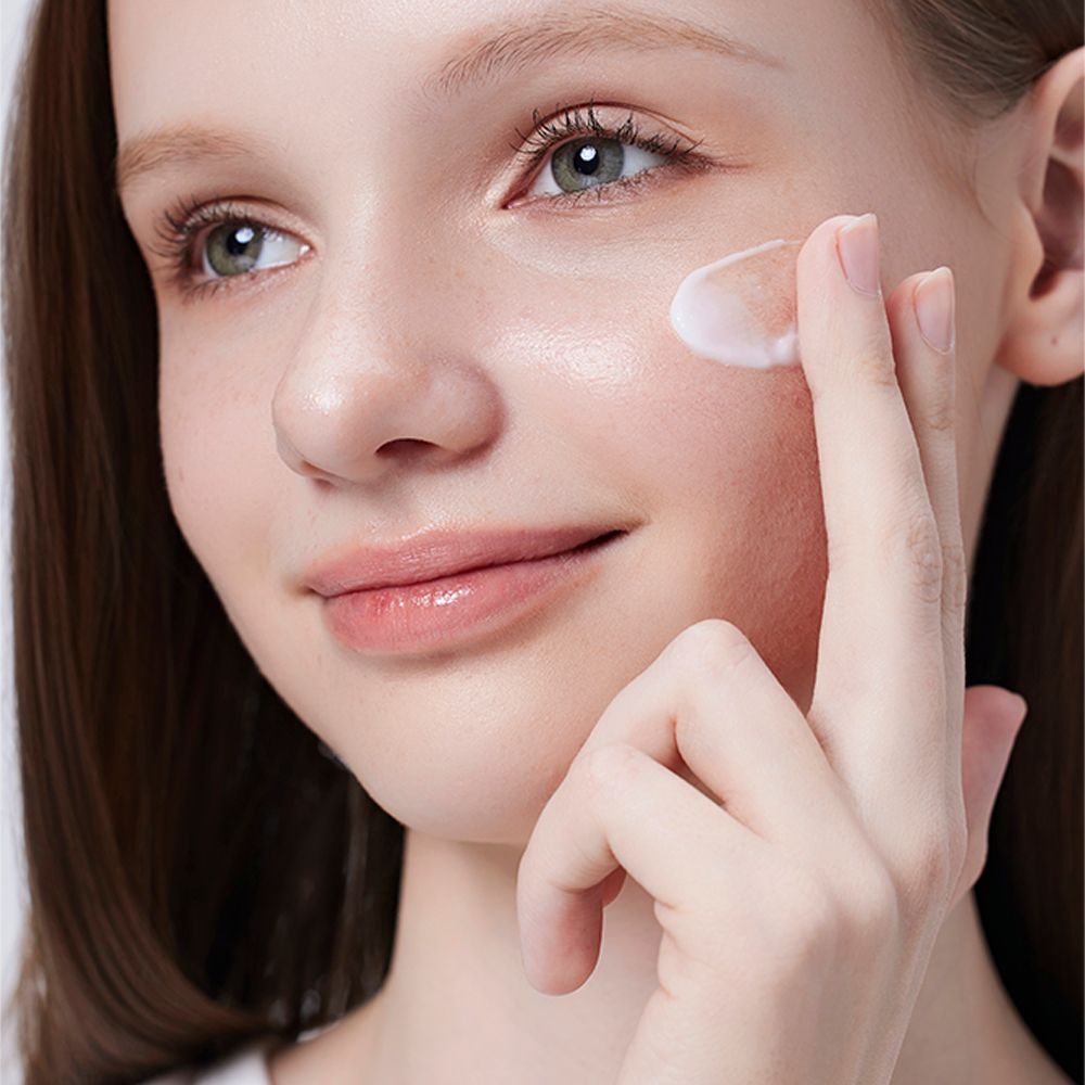 Una donna applica la crema idratante COSRX The Ceramide Skin Barrier sulla sua guancia.