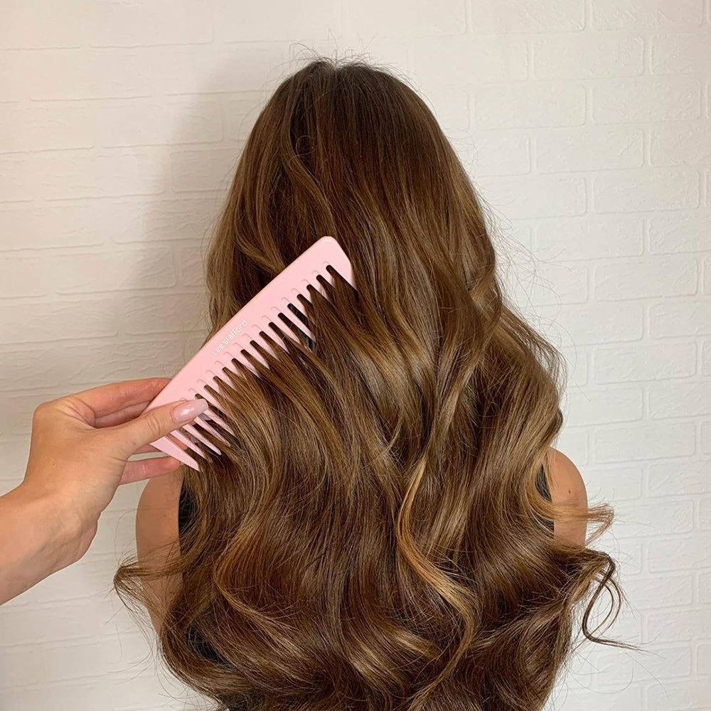 Un pettine rosa pallido a denti larghi usato tra lunghi capelli mossi.