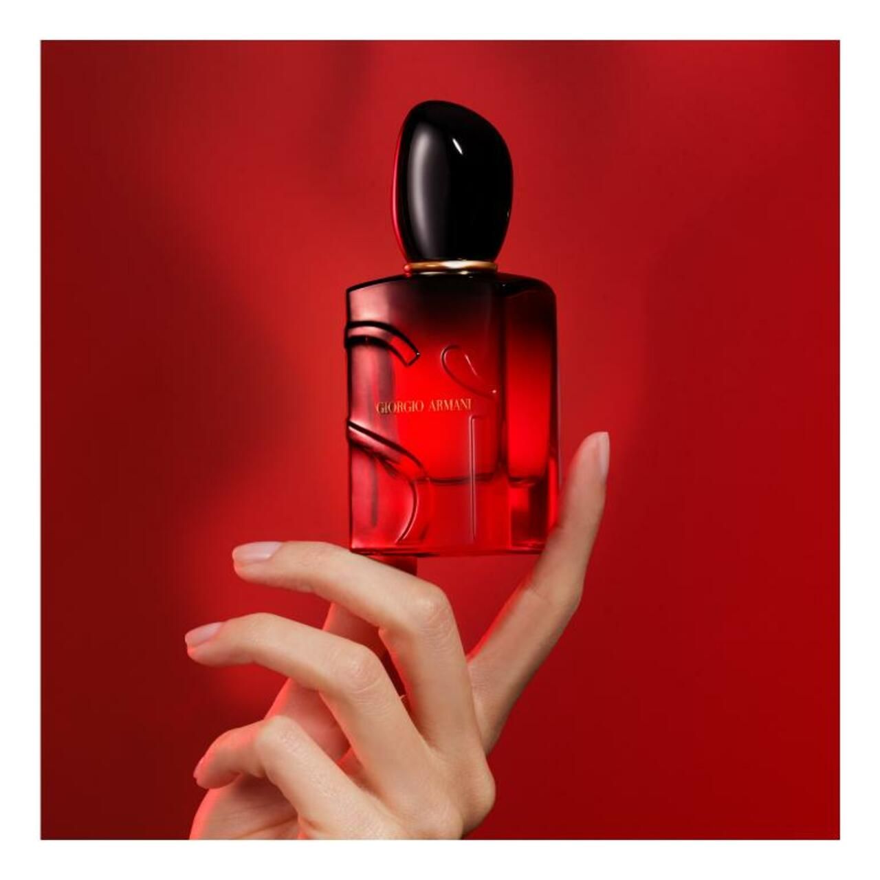 Flacone rosso Giorgio Armani Sì Passione Intense Eau de Parfum. Tappo nero. Tenuto in mano, su sfondo rosso.