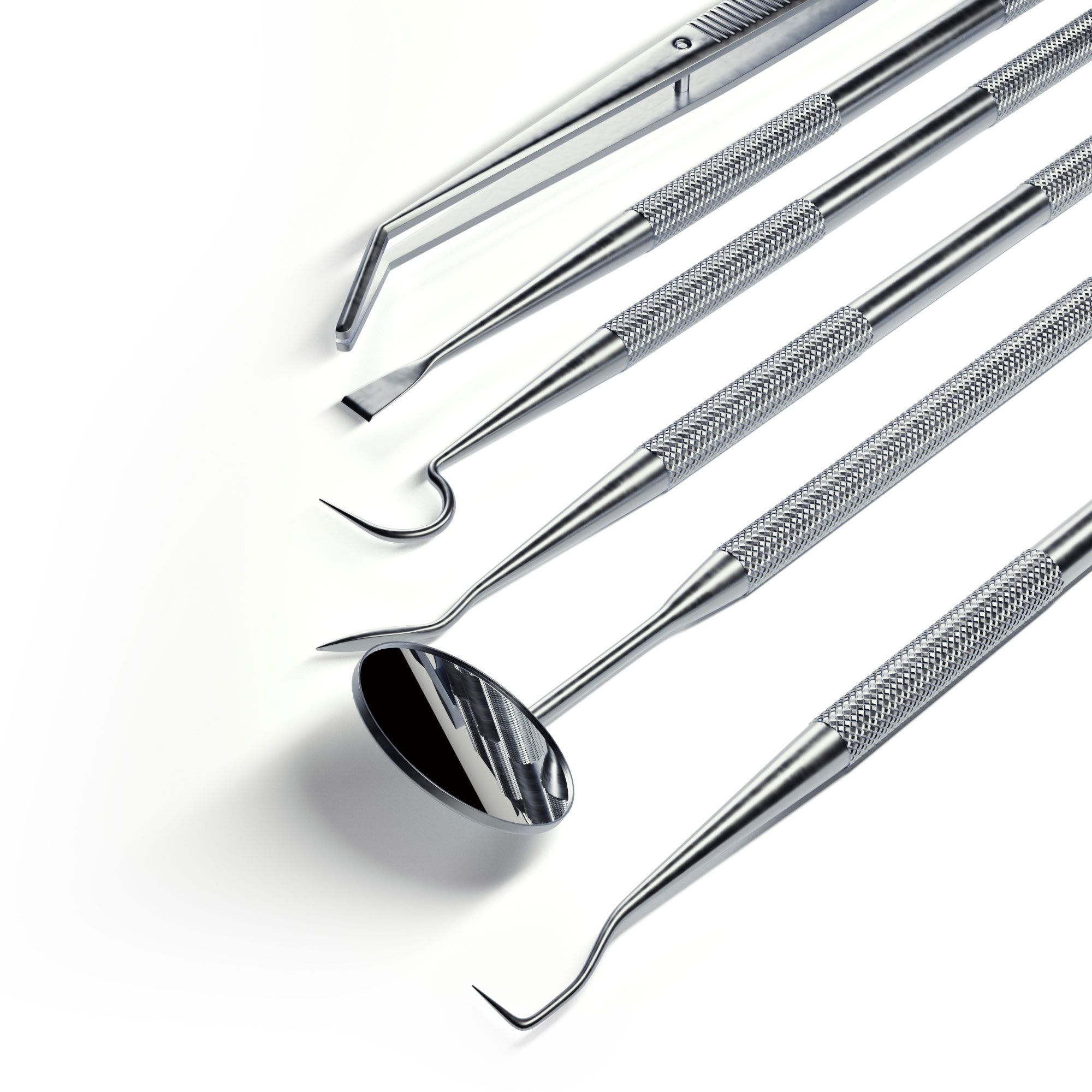 Primo piano di strumenti odontoiatrici argentati. Specchio, pinzette e vari strumenti con manici zigrinati. Su sfondo bianco.