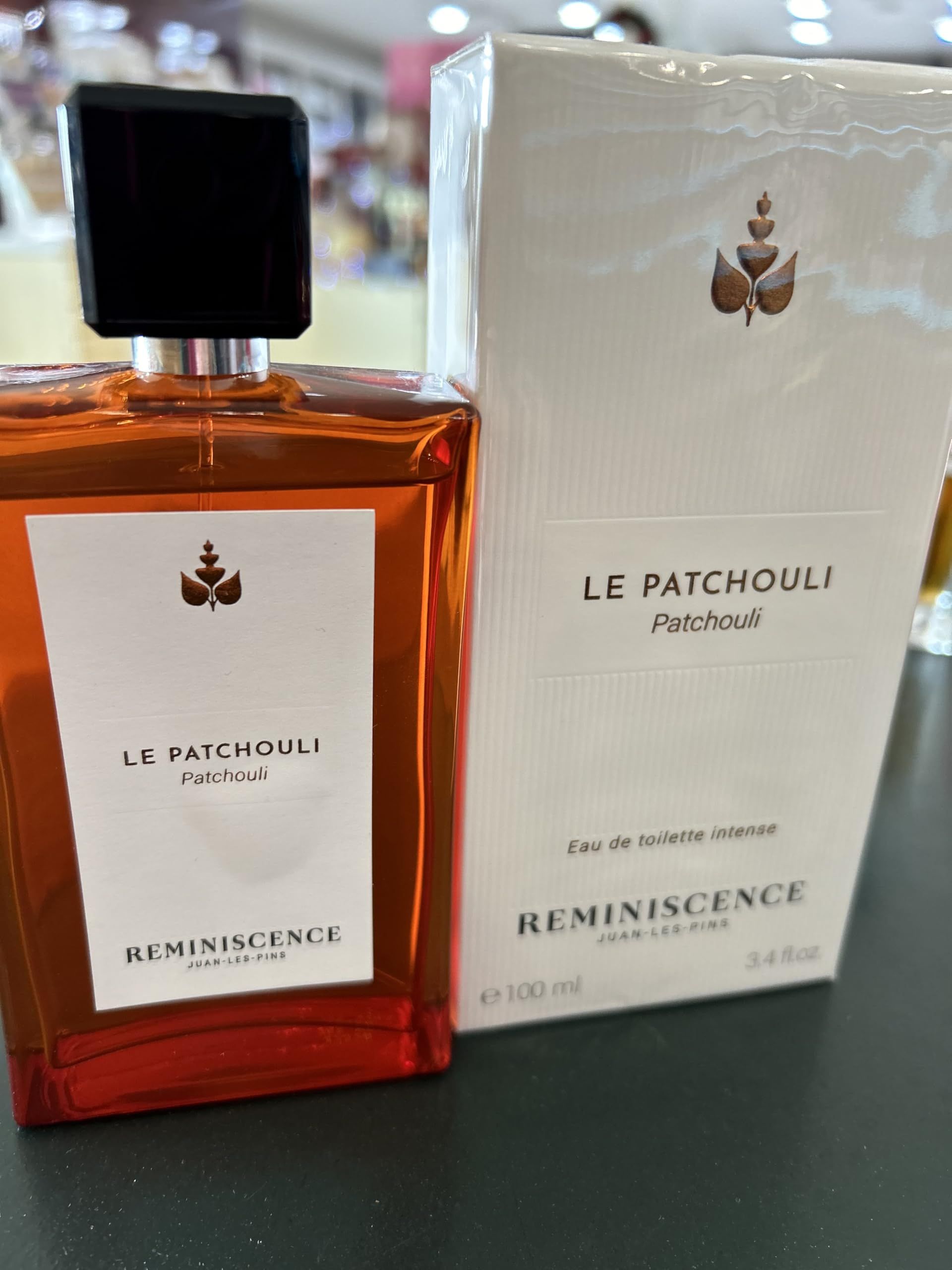 Flacone e confezione di Le Patchouli Eau de Toilette Intense Spray. Flacone con liquido marrone, accanto la confezione bianca.