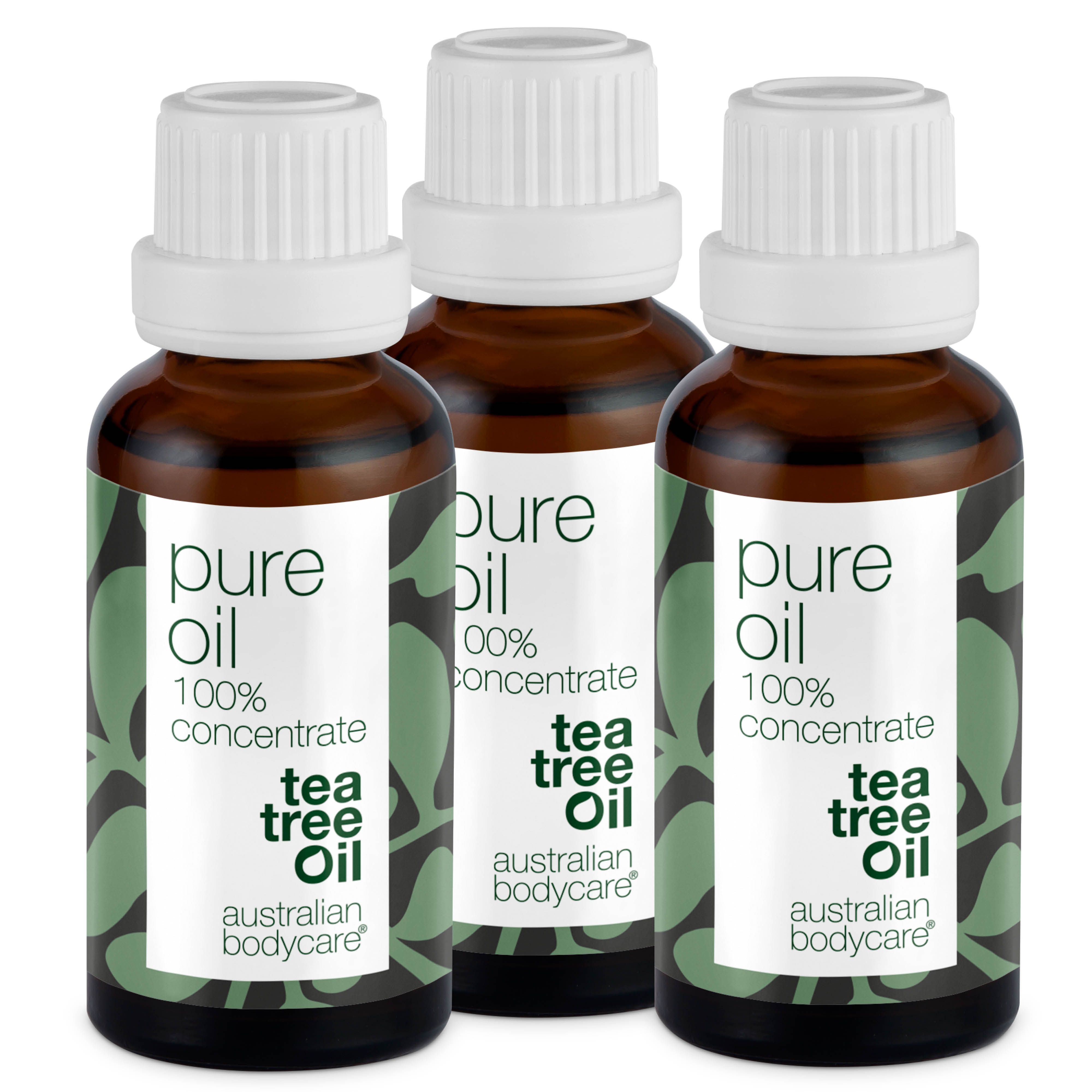 Tre bottiglie di olio di tea tree. Bottiglie di vetro marrone con tappo bianco. Scritta: Pure Oil, 100% Concentrate, Tea Tree Oil.