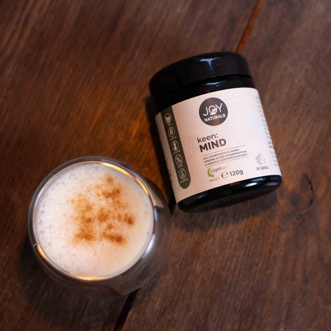 Barattolo marrone JOY NATURALS keen:MIND accanto a un bicchiere di bevanda. Scritta: 120g.