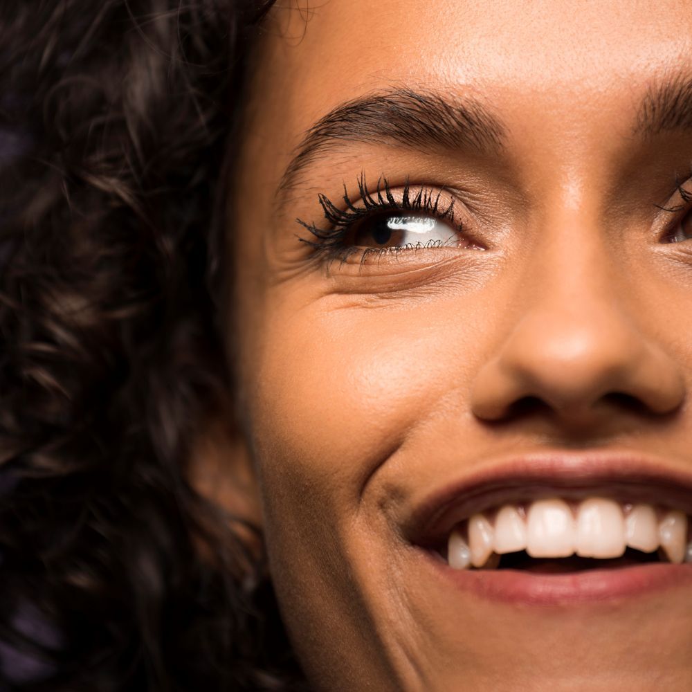 Primo piano di un viso sorridente con ciglia truccate. Tono della pelle, sopracciglia e occhi visibili.