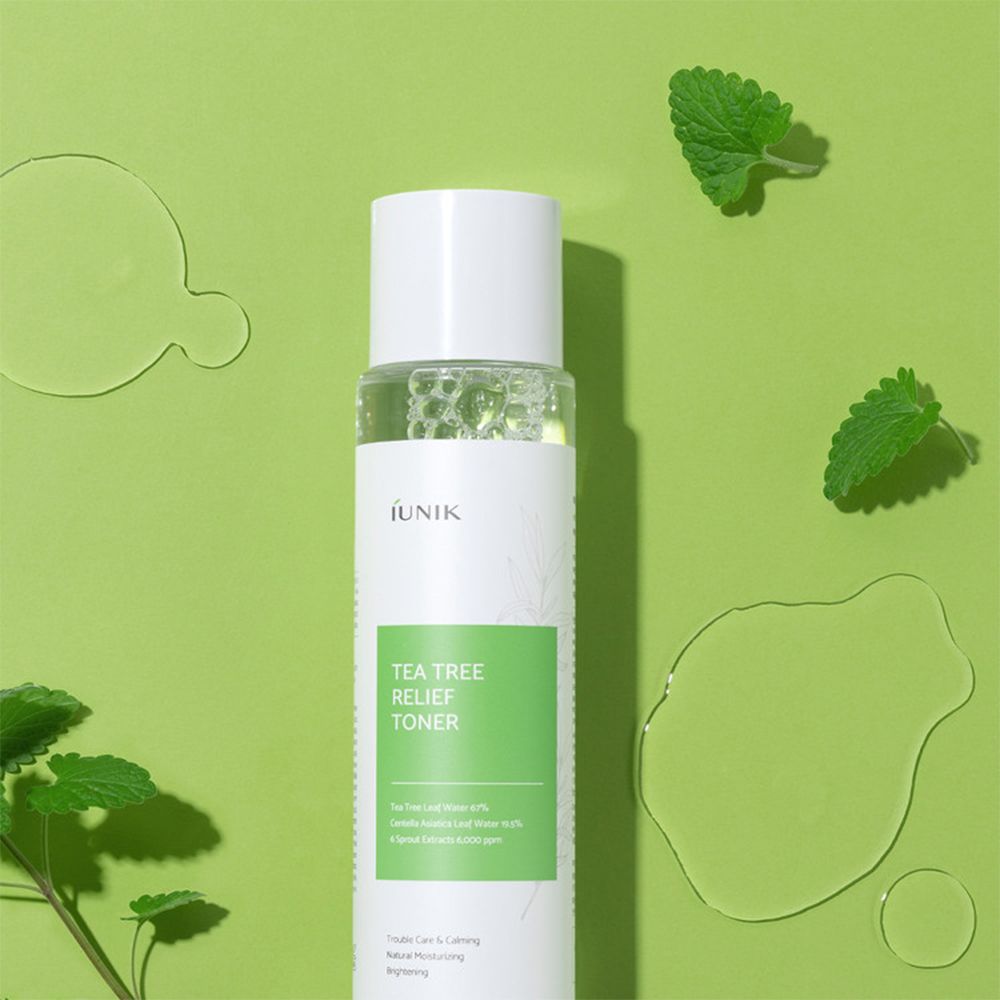 iUNIK Tea Tree Relief Toner su sfondo verde con gocce d'acqua e foglie. Liquido limpido in flacone trasparente.