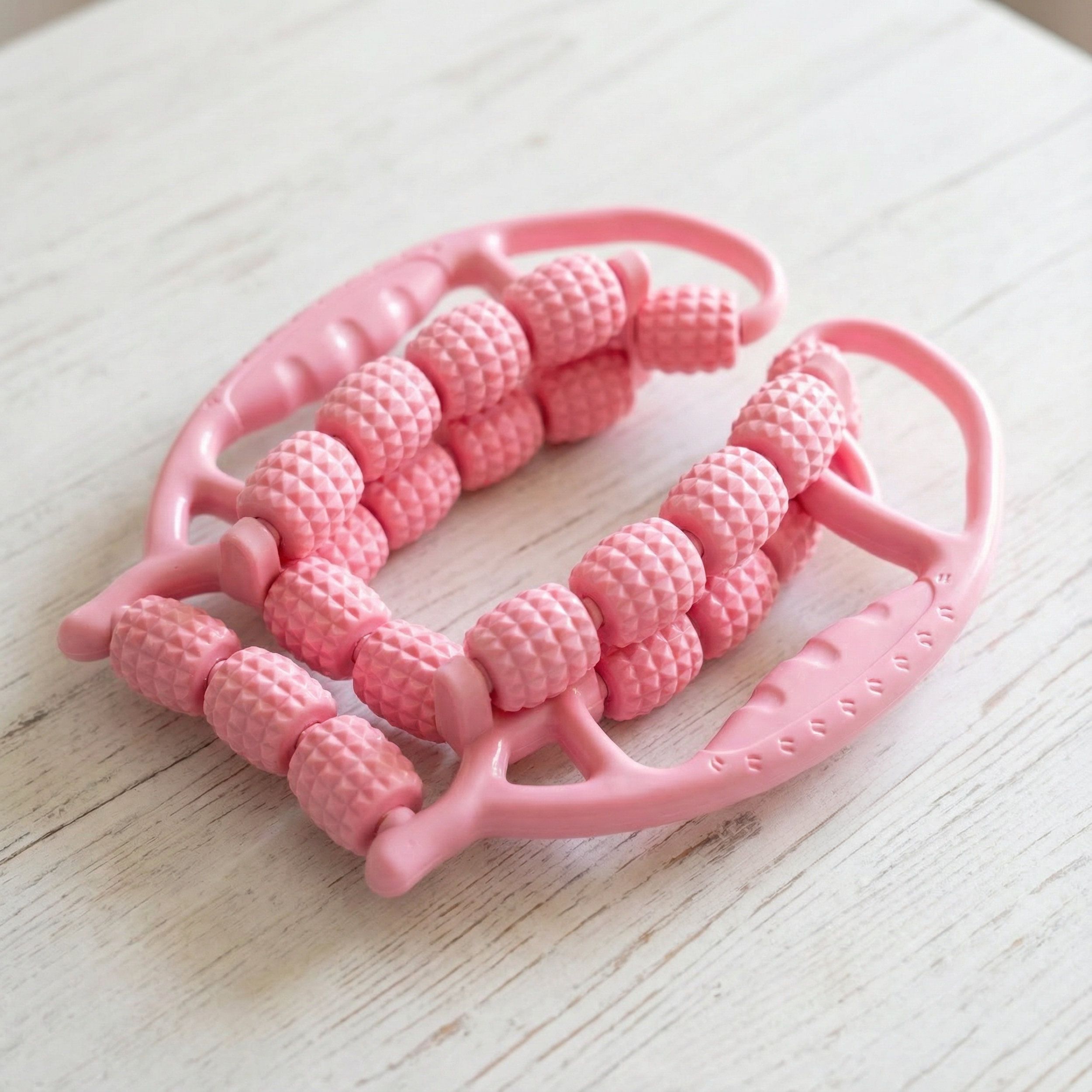 Rullo massaggiante rosa, primo piano. Diversi rulli con manici. Su fondo in legno chiaro.