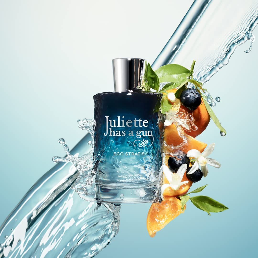 Flacone di vetro con tappo argentato, circondato da acqua, frutta e fiori. Scritta: Juliette has a gun EGO STRATIS.