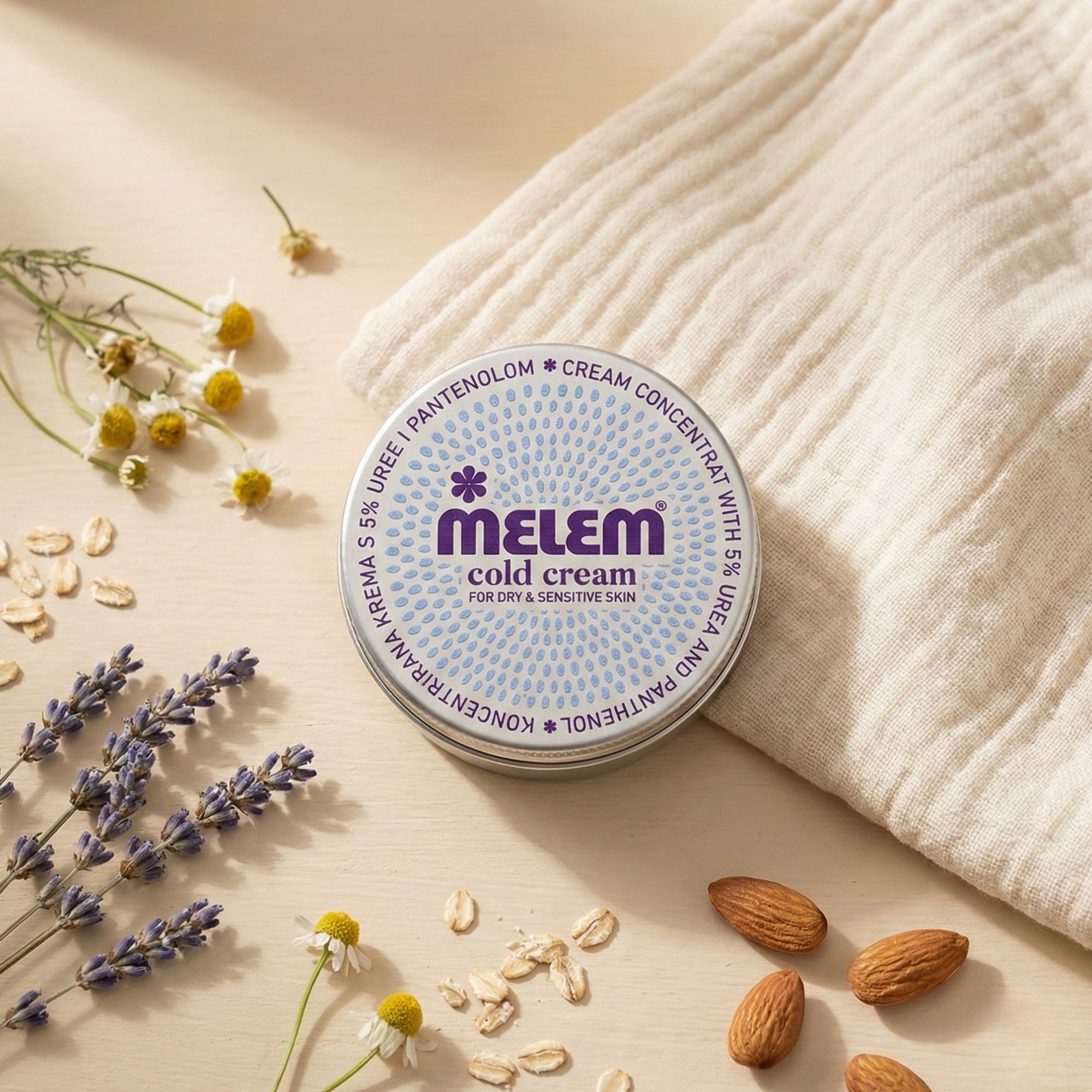 Barattolo rotondo Melem Cold Cream, circondato da lavanda, camomilla, fiocchi d'avena e mandorle.
