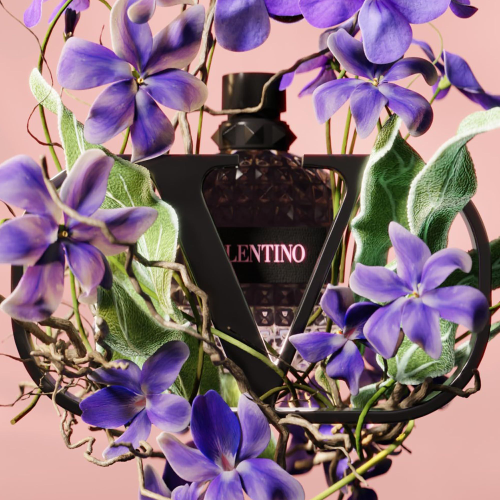 Flacone Valentino circondato da fiori e foglie. Sfondo rosa. Logo nero.