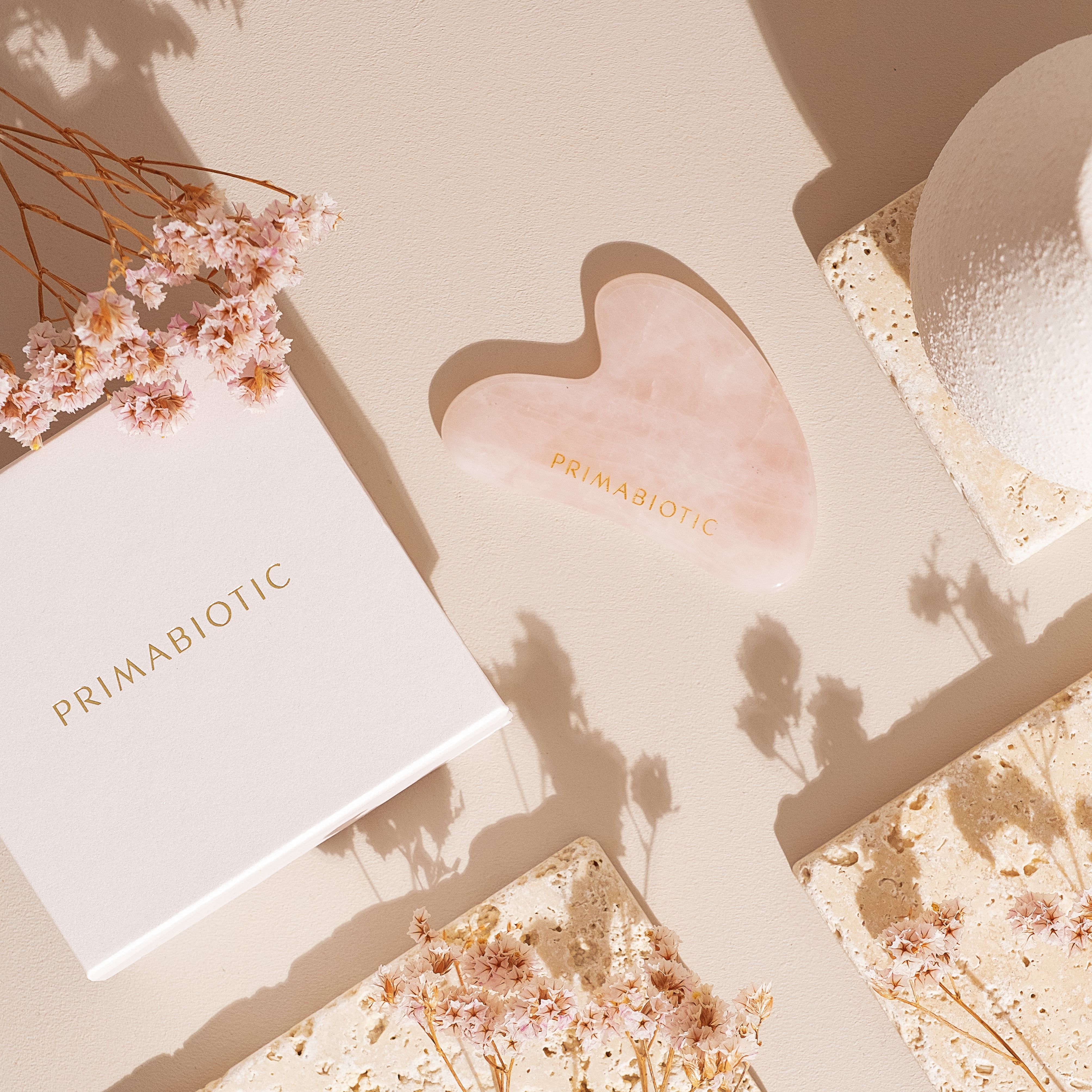 Pietra Gua Sha in quarzo rosa, a forma di cuore. Su sfondo beige con decorazioni e confezione.