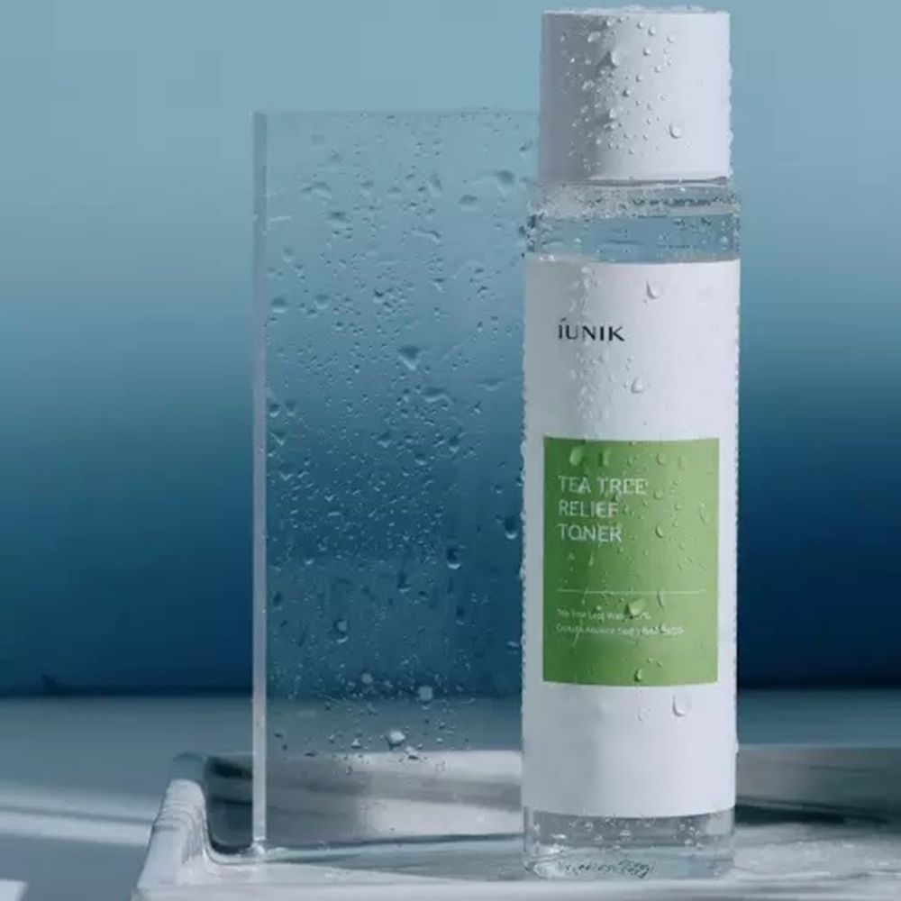 Flacone trasparente con tappo bianco, coperto di gocce d'acqua. Etichetta verde e bianca con testo: IUNIK, Tea Tree Relief Toner.