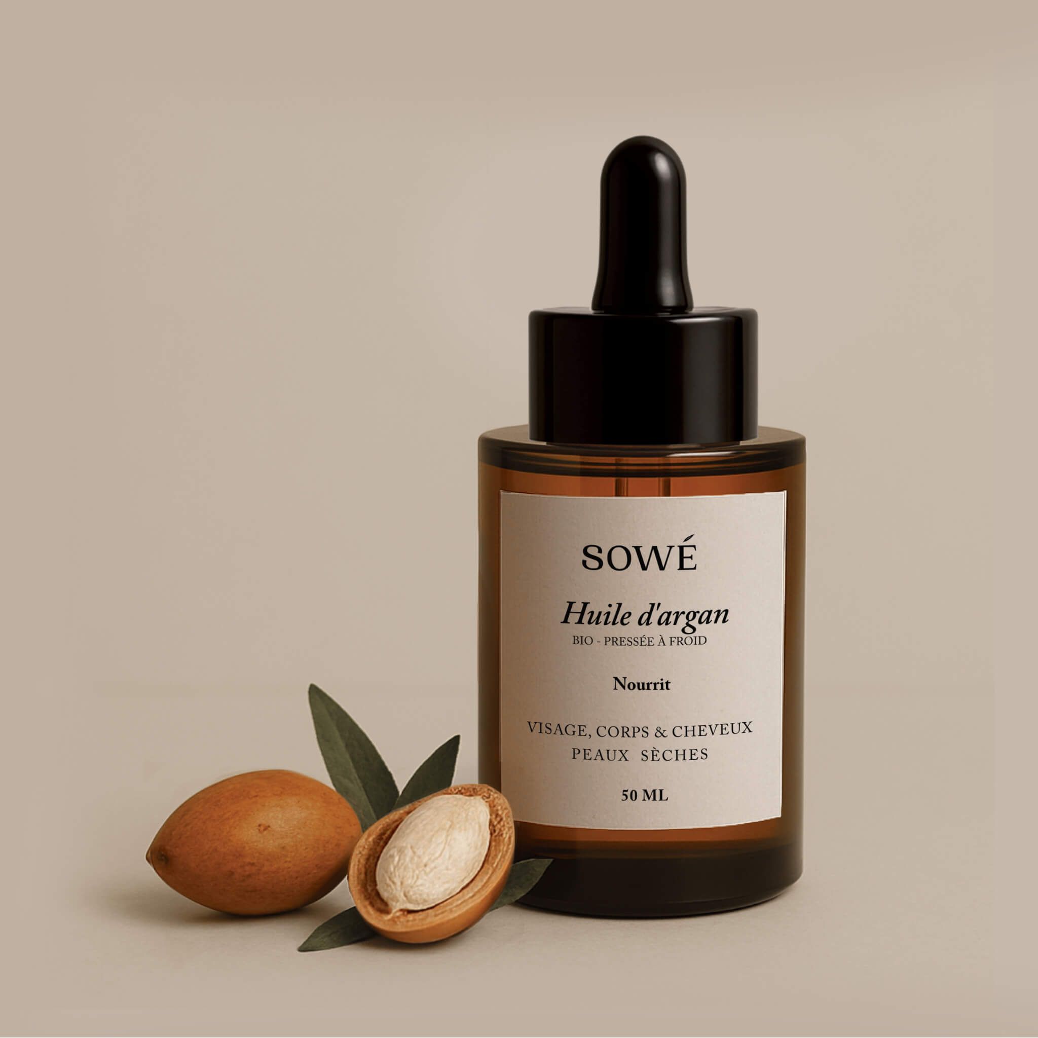 Flacone di vetro marrone con contagocce. Etichetta con testo: SOWÉ, Huile d'argan, Nourrit, Visage, corps & cheveux, peaux sèches. Frutti di argan accanto.