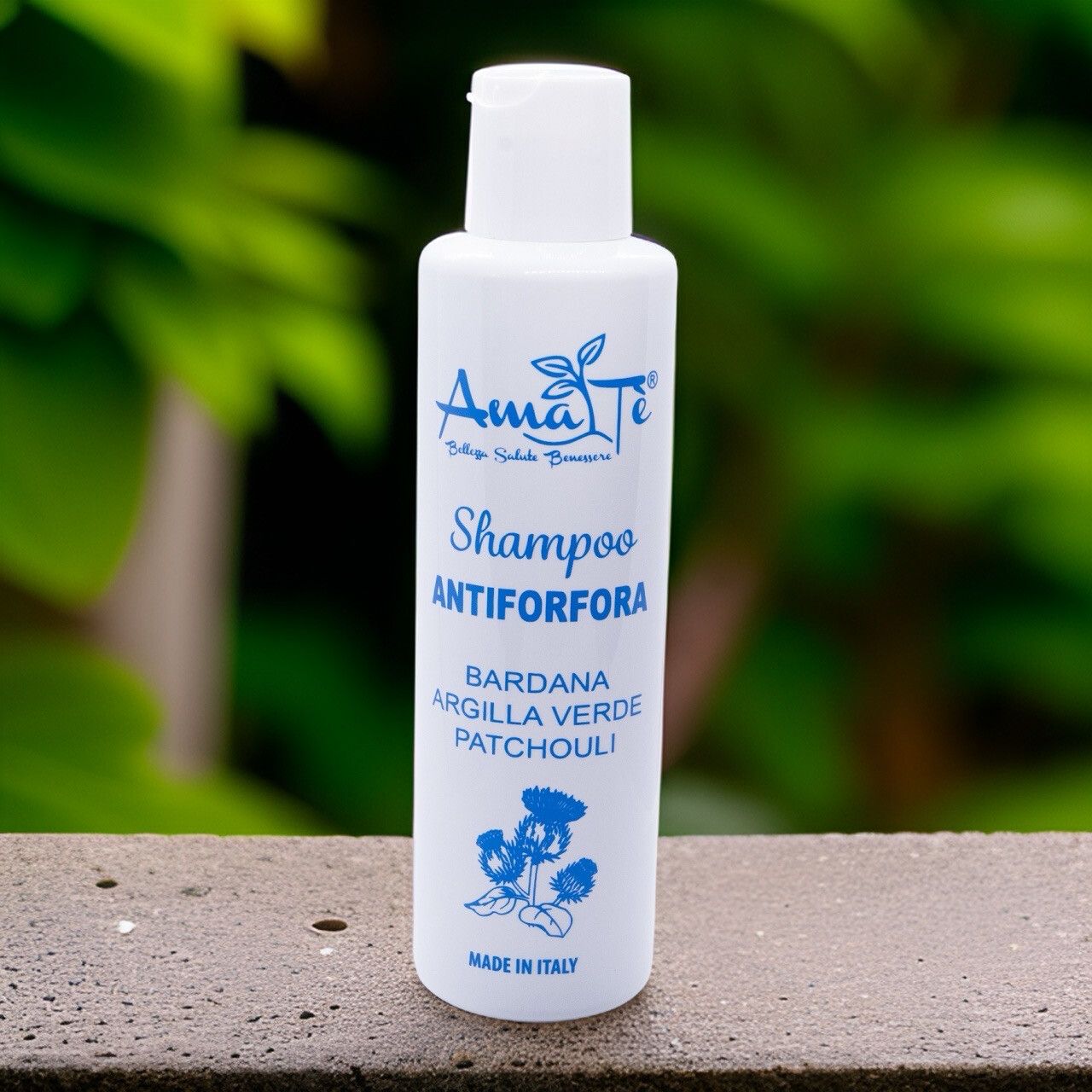 Flacone bianco con etichetta blu. Testo: Shampoo Antiforfora, ingredienti. Su pietra.