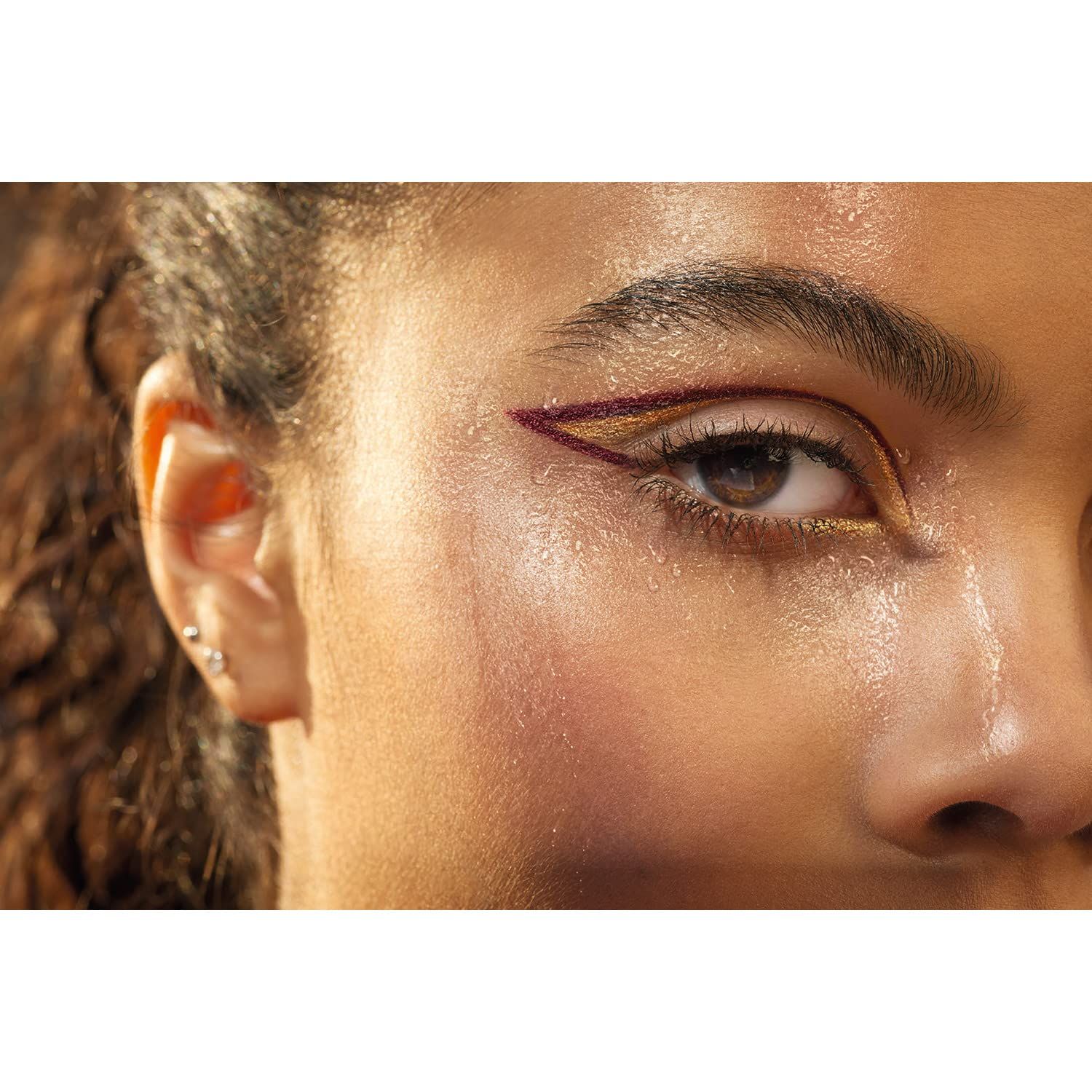 Primo piano di un occhio con eyeliner dorato e rosso. Pelle lucida.