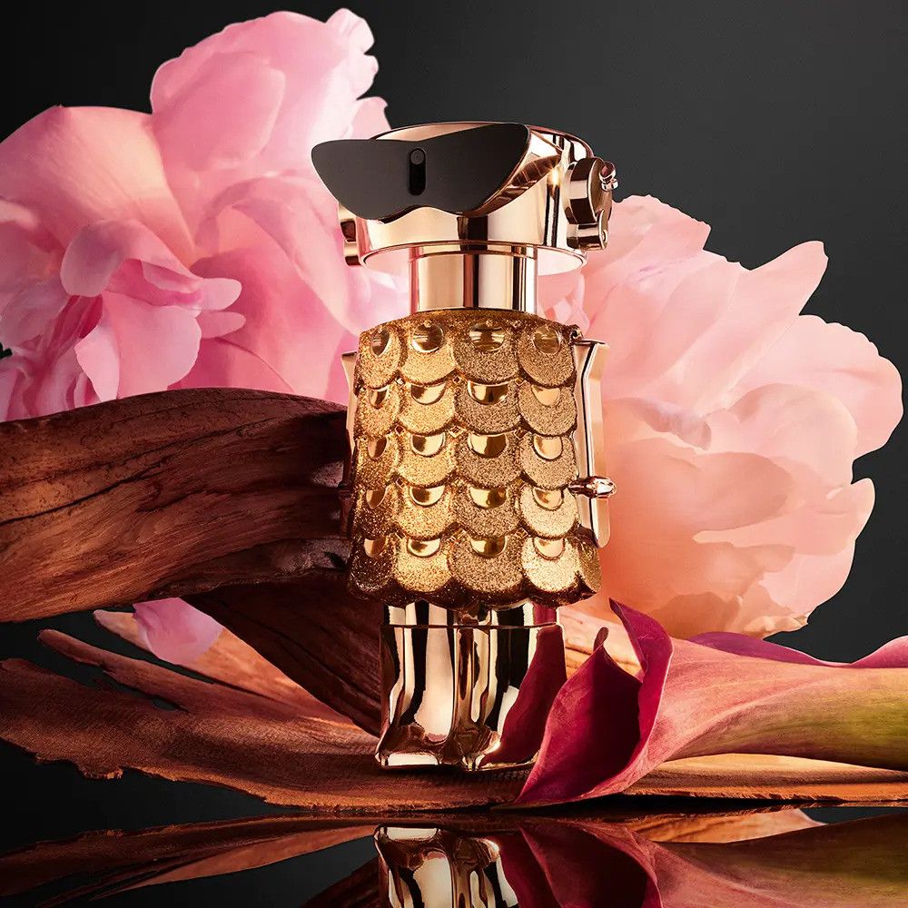 Flacone dorato con occhiali neri, circondato da fiori e legno. Design del flacone: robot.