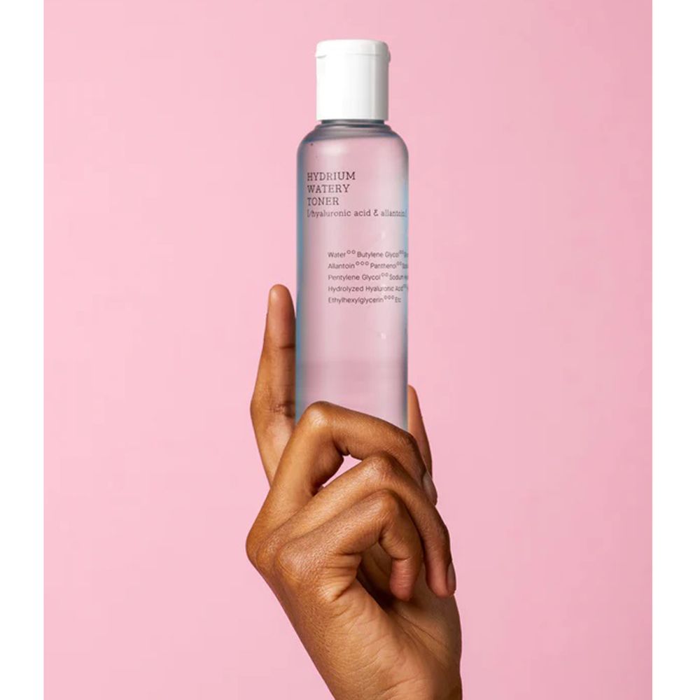 Flacone di toner per la pelle, liquido blu, tappo bianco. Mano che tiene il flacone. Scritte: HYDRIUM WATERY TONER, ingredienti.