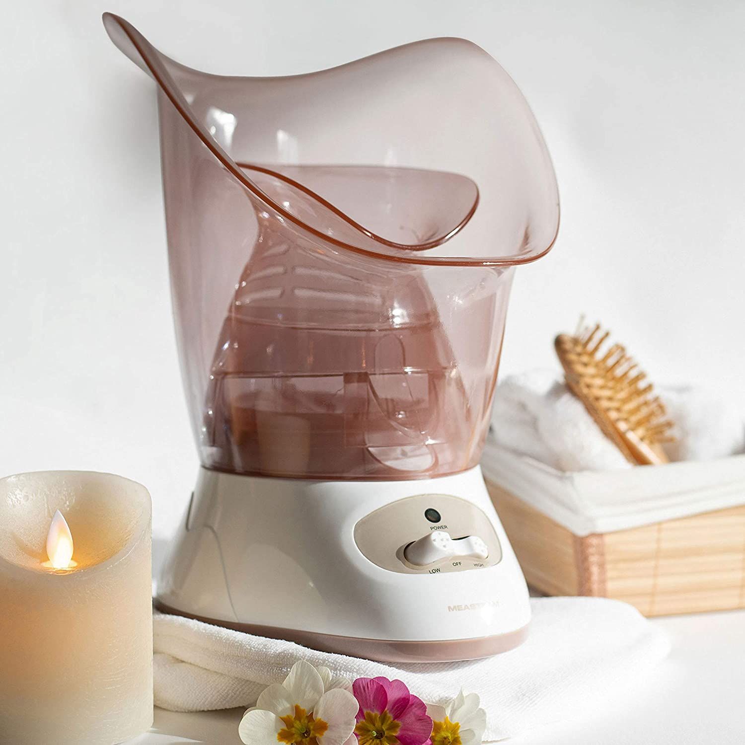 Sauna facciale bianca e rosa. Candela, asciugamano e spazzola sullo sfondo.