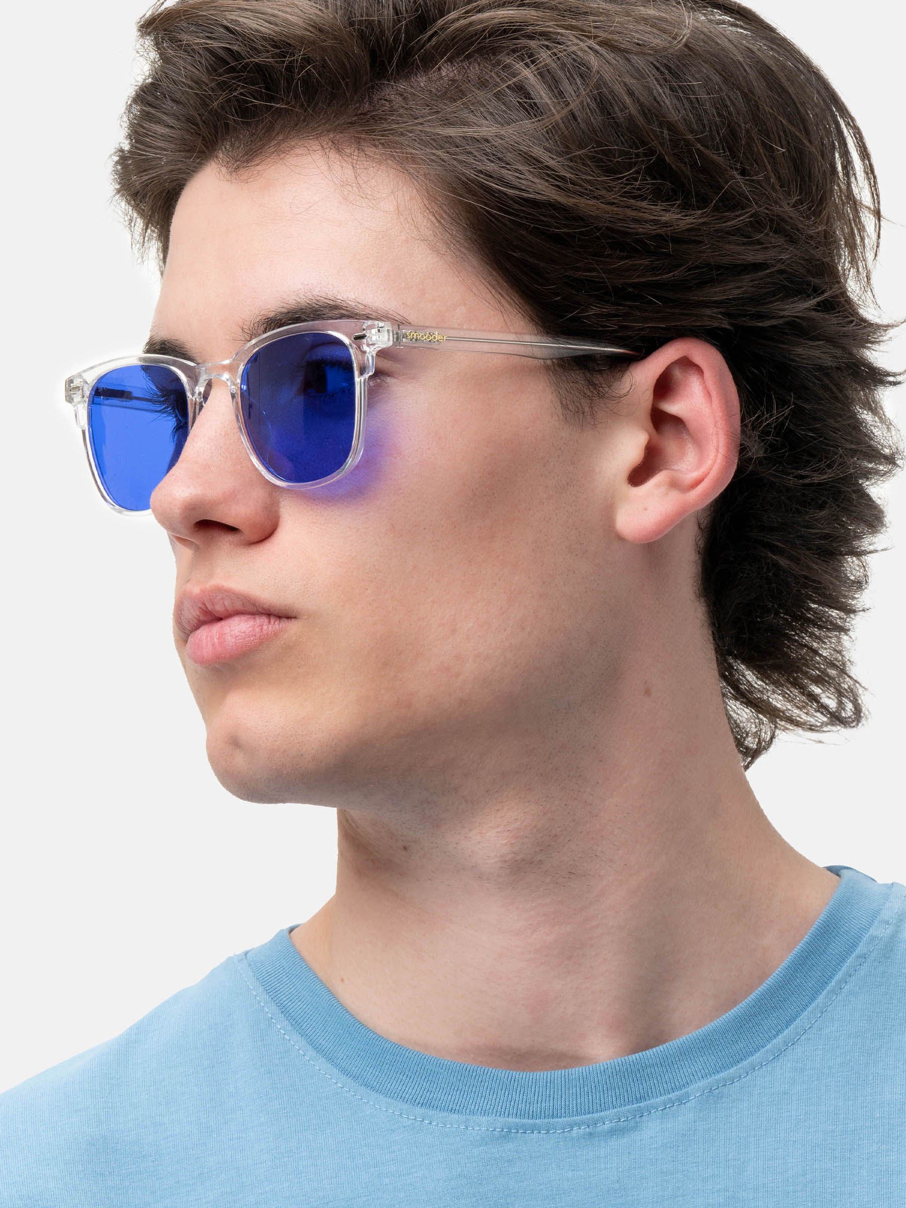 Uomo con occhiali da sole con montatura trasparente e lenti blu. Logo Smooder visibile.