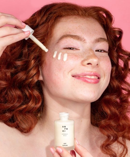 Donna applica siero. Flacone con tappo bianco e scritta. Siero sulla pelle. Sfondo rosa.