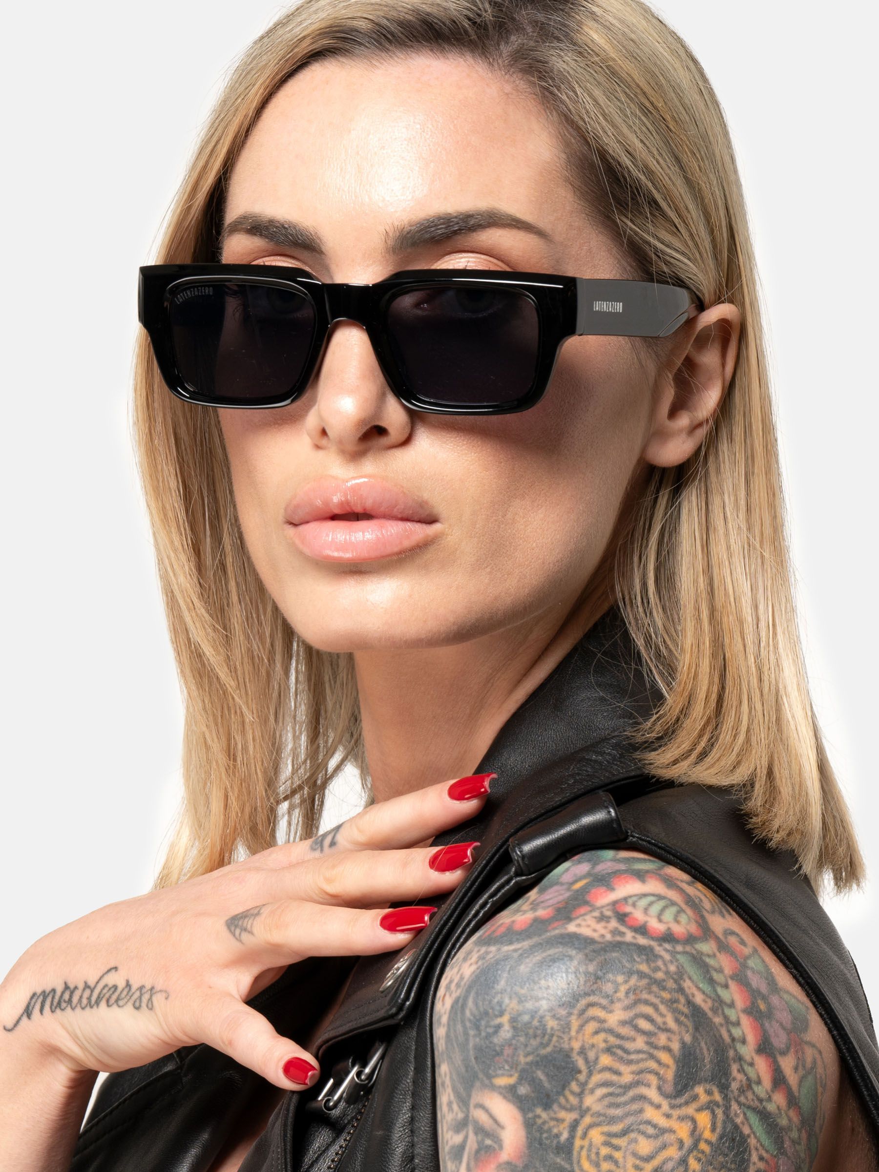 Donna con occhiali da sole neri. Lenti rettangolari e montatura nera. 'Latenzazero' sull'asta.