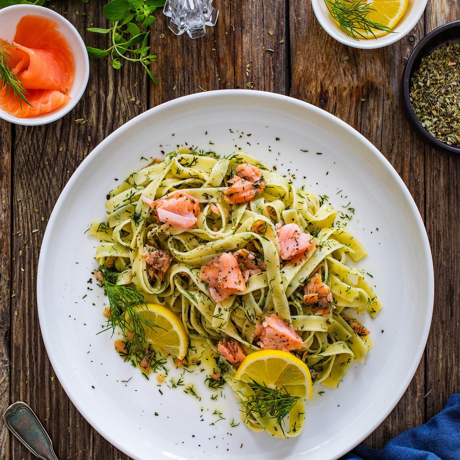 Tagliatelle con salmone, aneto e fette di limone su un piatto bianco. Sfondo in legno.