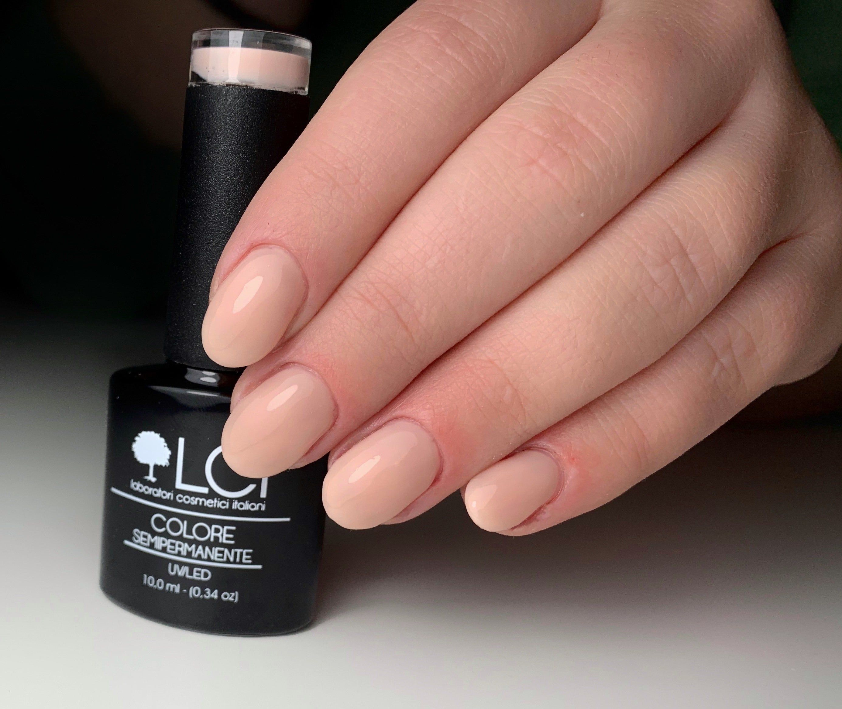 Mano con unghie smaltate rosa nude. Flacone di smalto accanto. Marchio LCI Cosmetics.