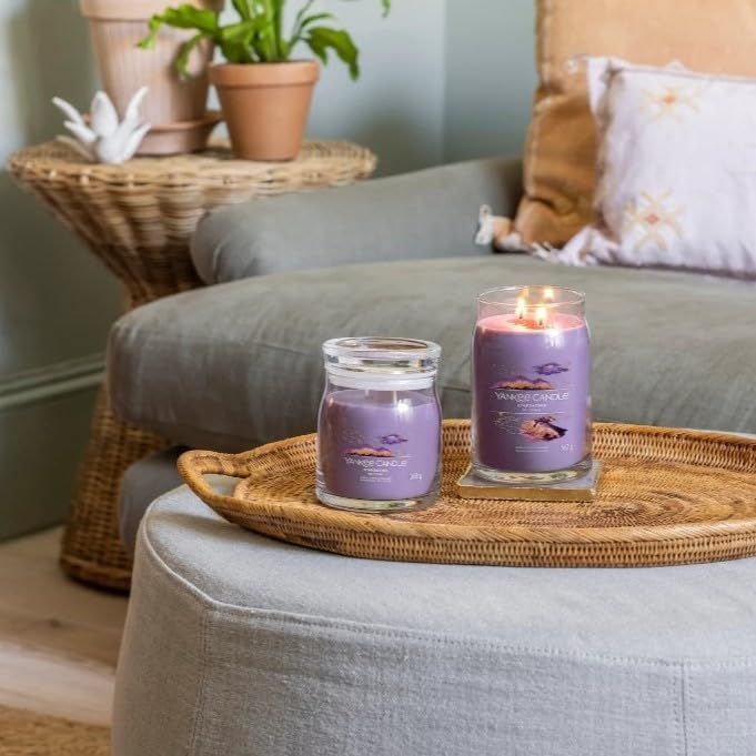 Due candele su un vassoio. Una brucia. Scritta: Yankee Candle. Ambiente: poltrona, tavolo, cuscino.