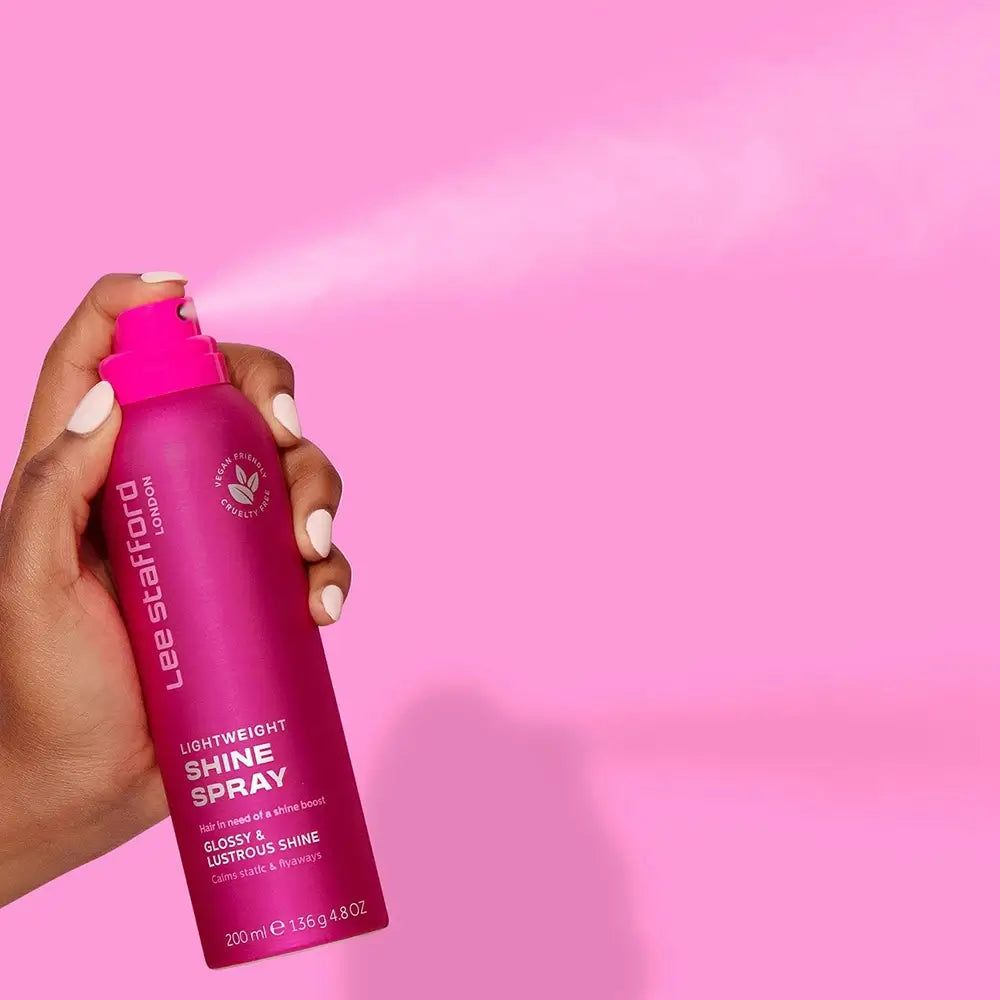 Mano che spruzza lo spray lucidante leggero Lee Stafford da un flacone rosa.