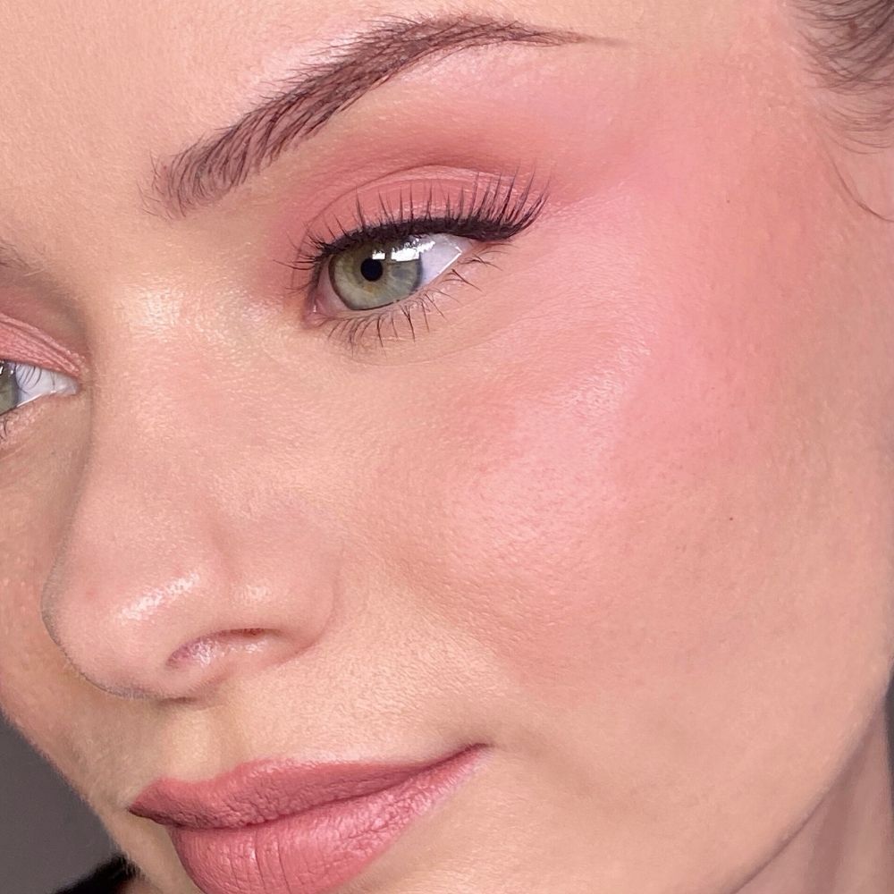 Primo piano di un viso con trucco rosa su occhi e guance. Occhi verdi, ciglia finte.