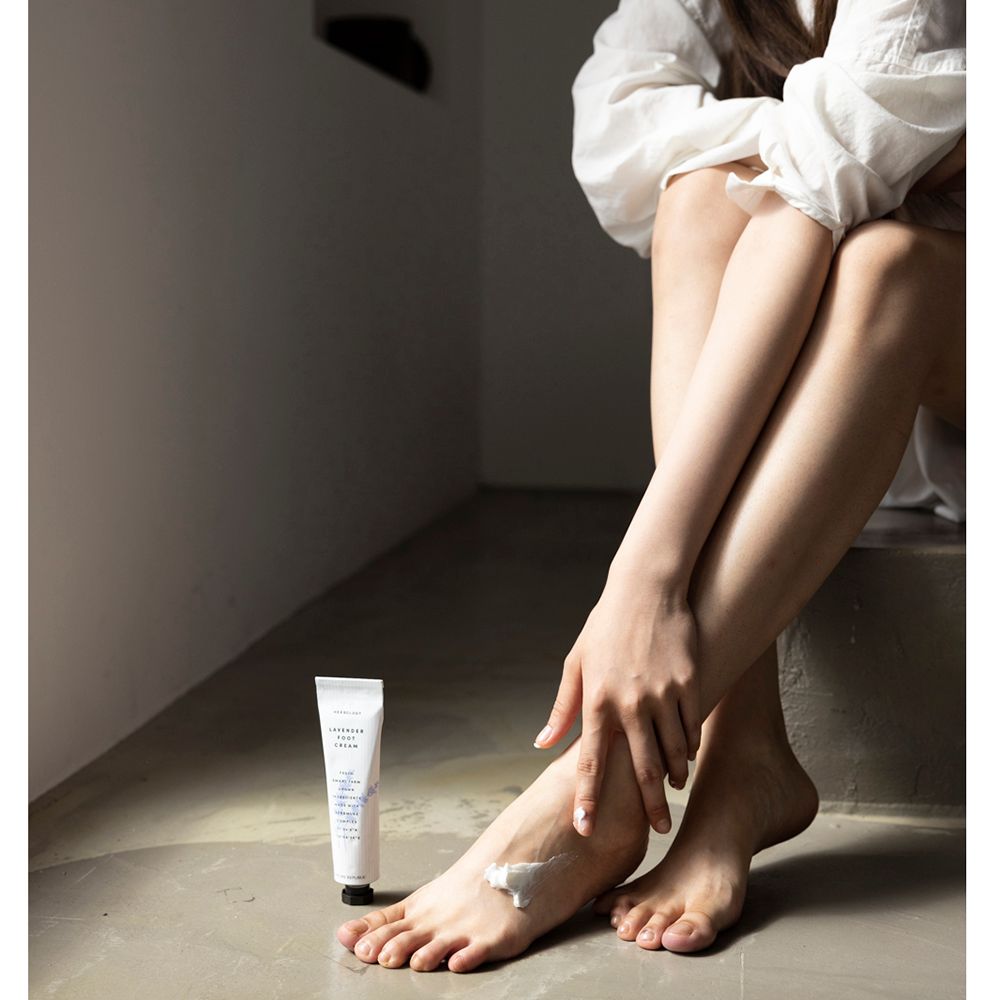 Persona con piedi e tubo di crema per piedi. Crema applicata sul piede. Marchio: NATURE REPUBLIC. Testo: Herbology, Lavender Foot Cream.