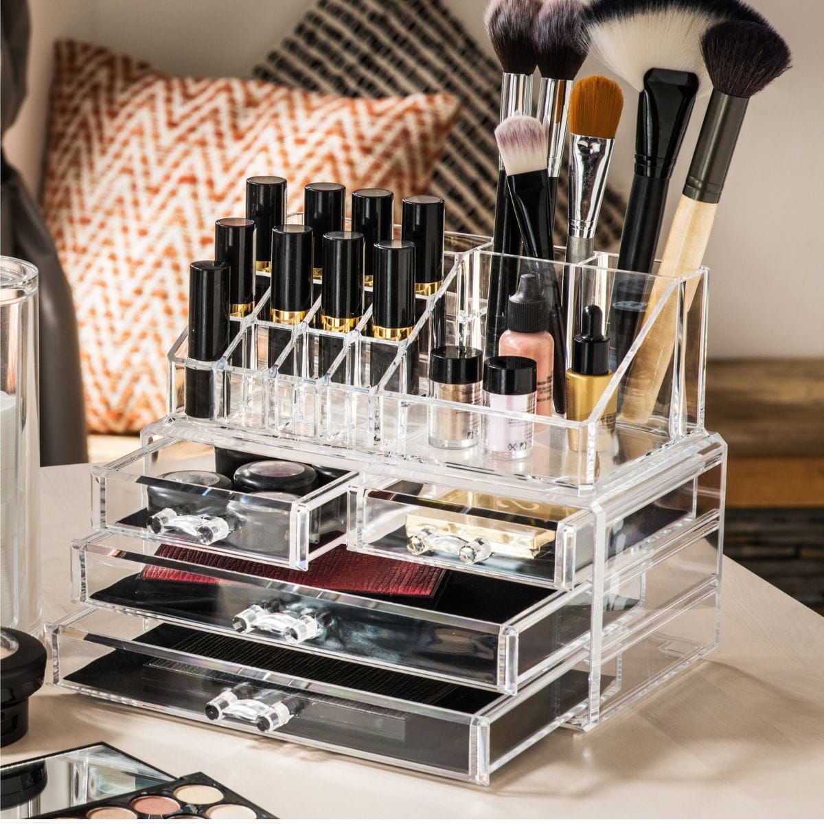 Organizzatore cosmetico trasparente in acrilico con scomparti multipli e cassetti, riempito di trucchi e pennelli.