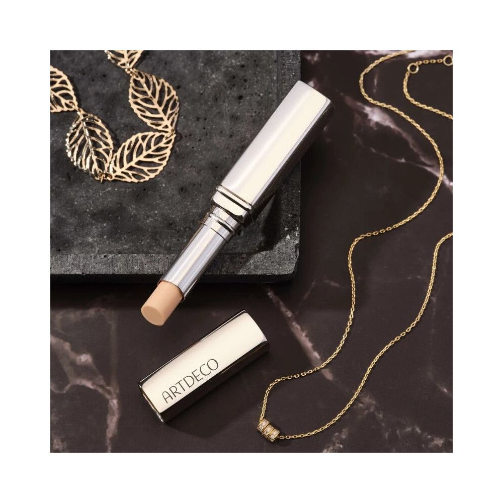 Un rossetto argento con cappuccio aperto e prodotto. Collane d'oro sono su una superficie scura.