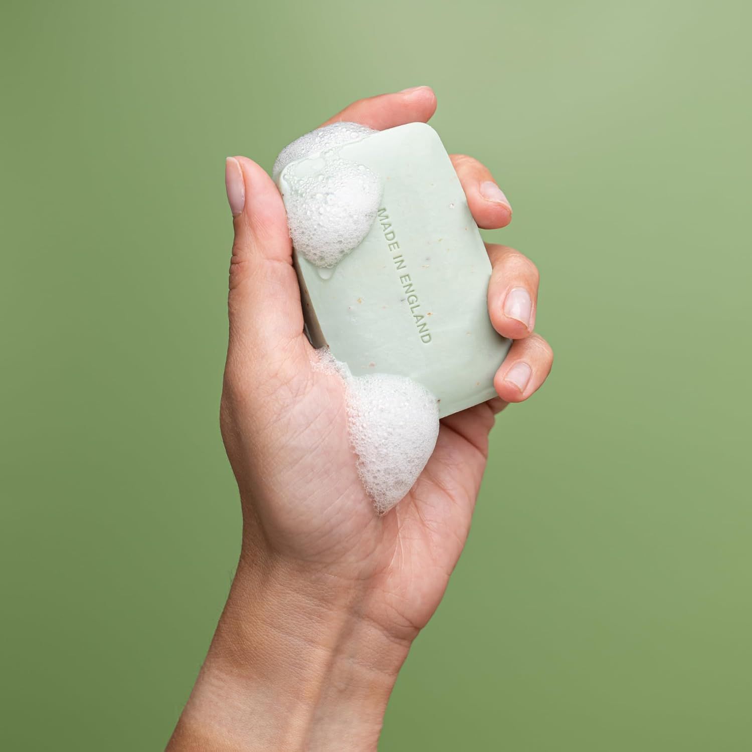 Mano che tiene una saponetta verde con schiuma. Scritta: MADE IN ENGLAND.