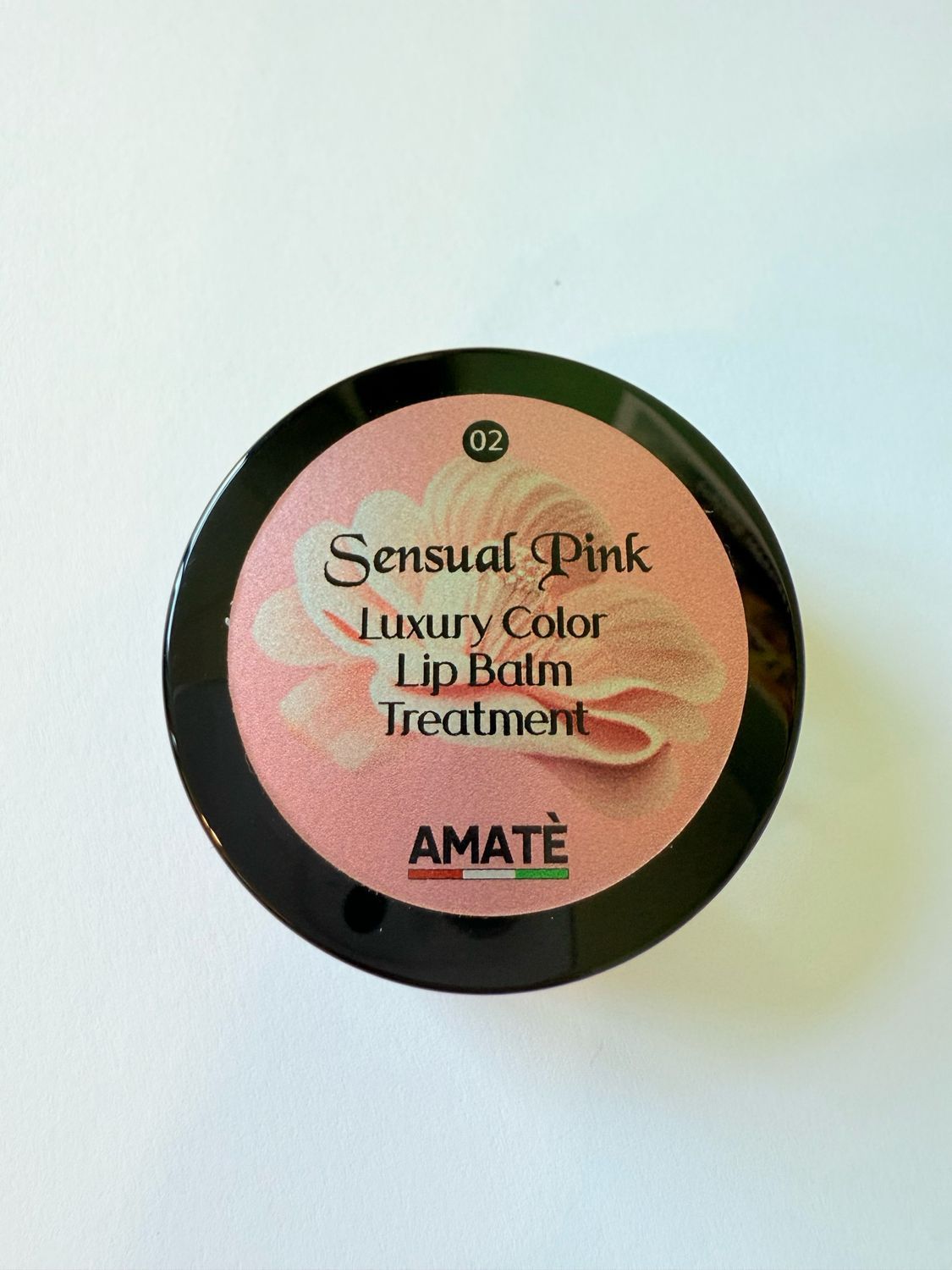 Vasetto rotondo con coperchio nero. Sul coperchio, si legge "Sensual Pink Luxury Color Lip Balm Treatment" e "AMATÈ".