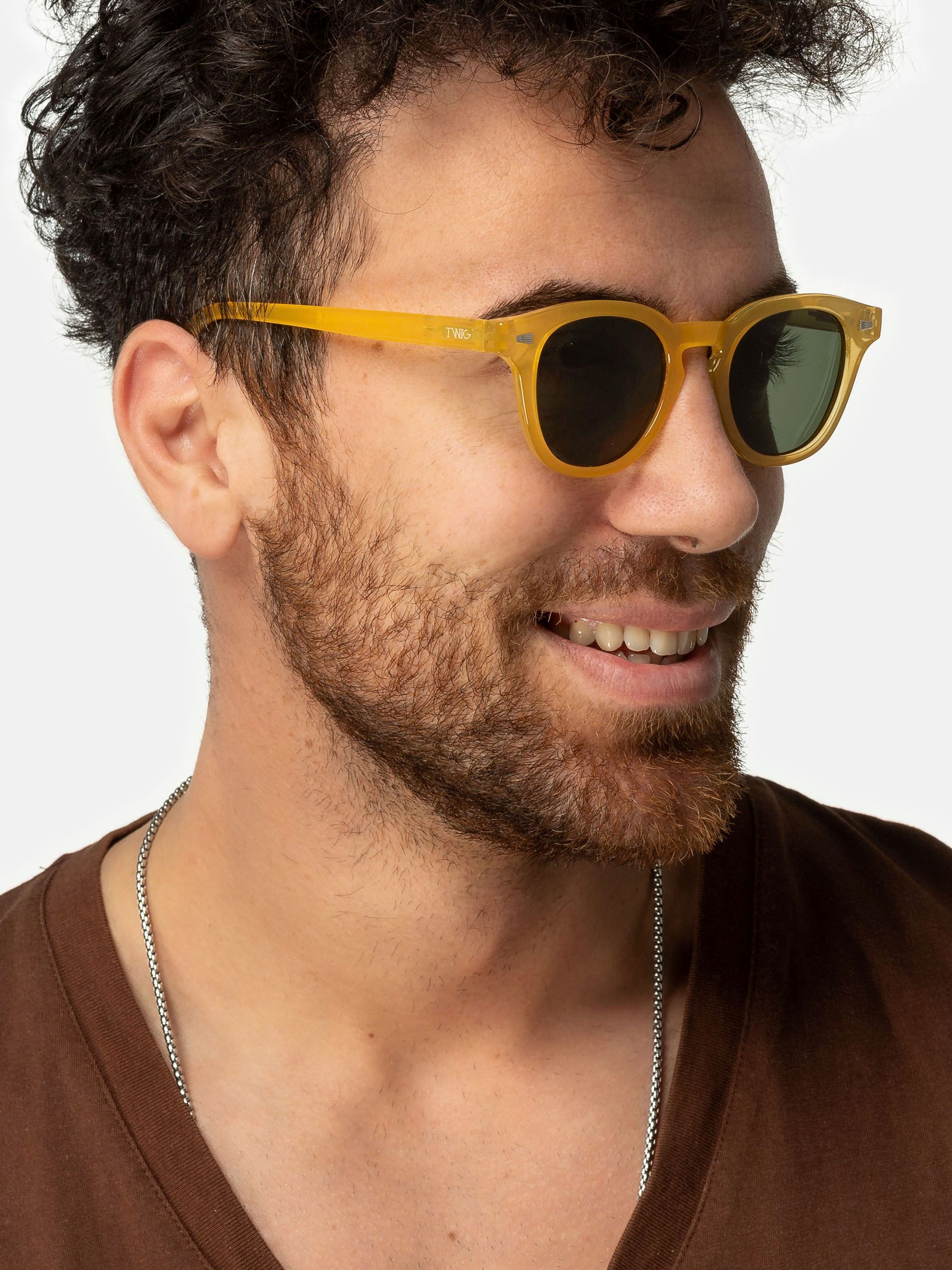 Uomo con occhiali da sole gialli. Primo piano. Sorridente. Collana visibile.