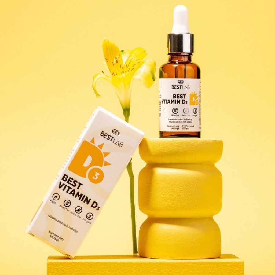 Flacone e scatola Best Vitamin D3 su piedistallo giallo con fiore. Vegano, senza glutine, senza lattosio, senza OGM.