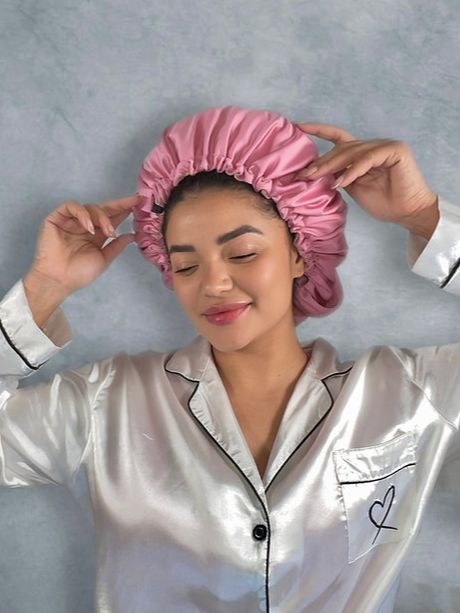 Persona indossa cuffia in seta rosa. Indossa camicia bianca con profili neri.