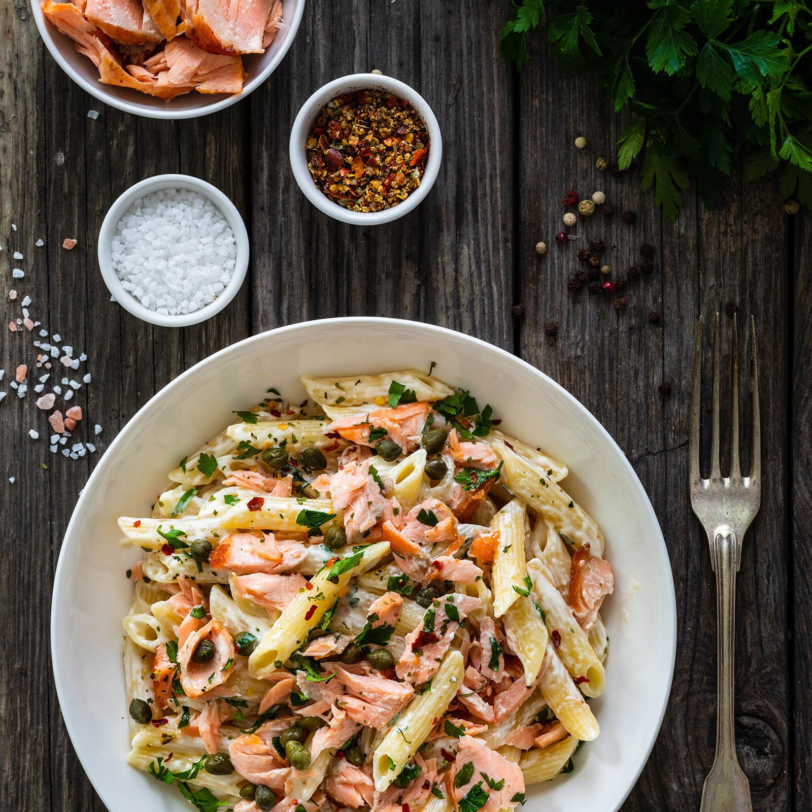 Ciotola di penne rigate con salmone, capperi ed erbe. Servito con sale e spezie.