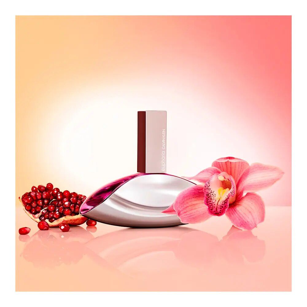 Flacone di profumo con melograno e orchidea. Flacone: ovale, argentato con contenuto rosa. Orchidea: rosa. Sfondo: arancione.
