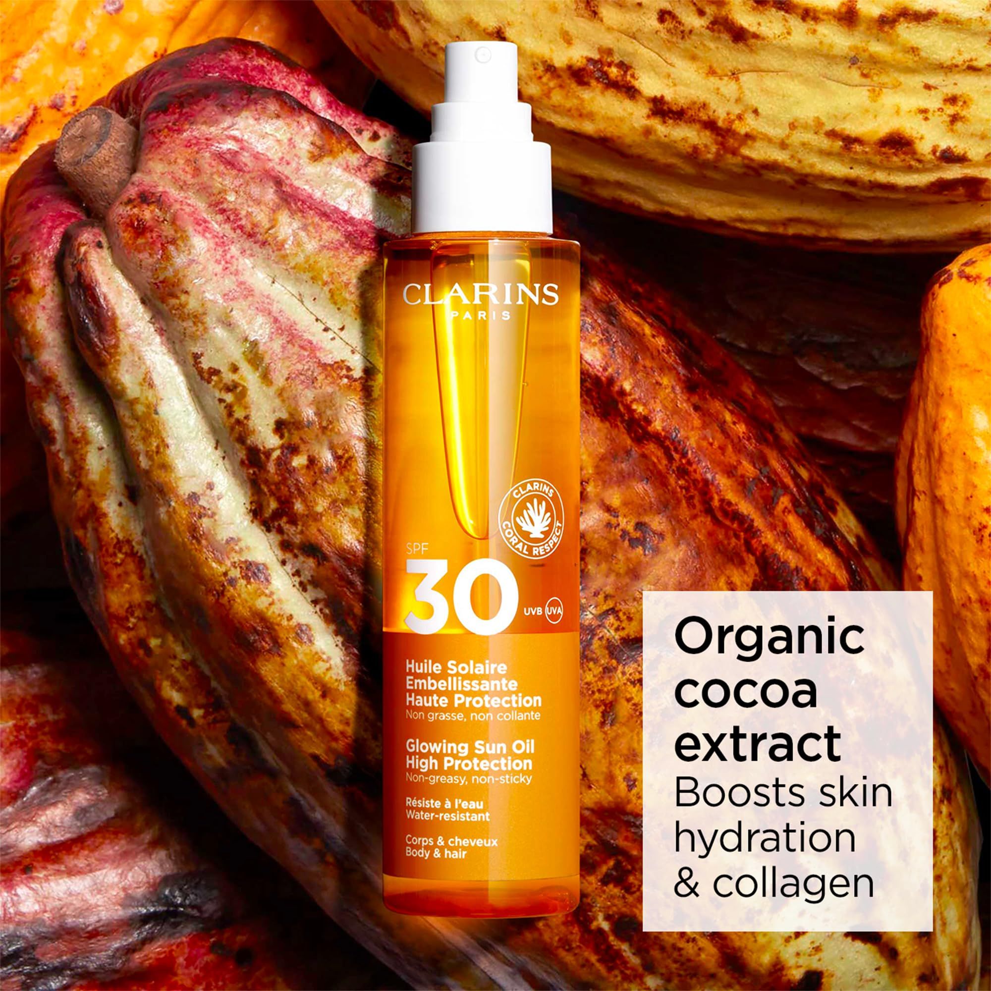 Spray olio solare davanti a fave di cacao. Flacone giallo con SPF 30. Logo Clarins. Testo: Organic Cocoa Extract.