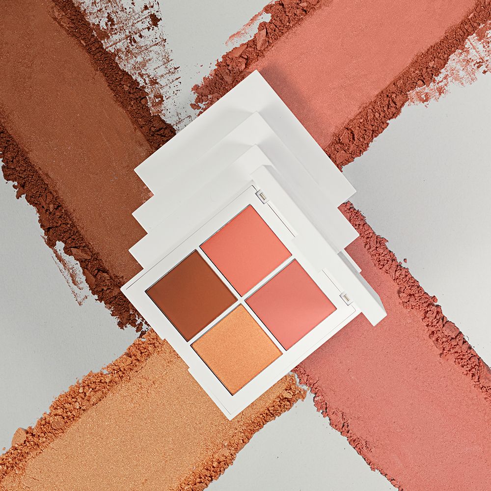 Palette trucco con quattro tonalità su sfondo bianco, circondata da strisce di polvere. Confezione bianca.