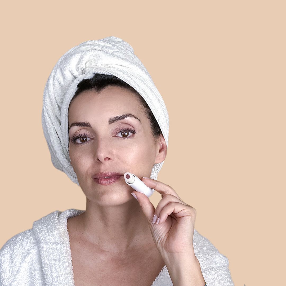 Donna tiene burrocacao davanti alle labbra. Indossa un asciugamano bianco sulla testa e un accappatoio.