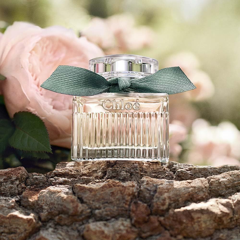 Flacone in vetro con nastro verde su tronco d'albero. Fiori di rosa sullo sfondo.