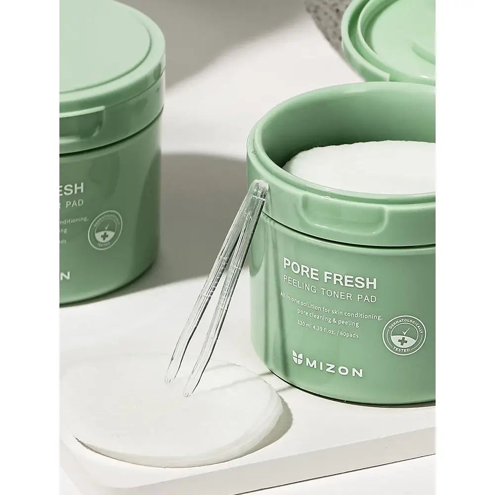 Barattolo verde con dischetti tonici, pinzetta trasparente, dischetto accanto. Scritta: Pore Fresh Peeling Toner Pad. Marchio: MIZON.