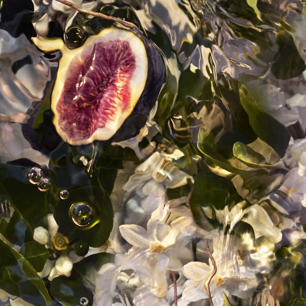 Primo piano di un fico a metà in acqua, circondato da fiori e foglie. Dettagli del frutto visibili.