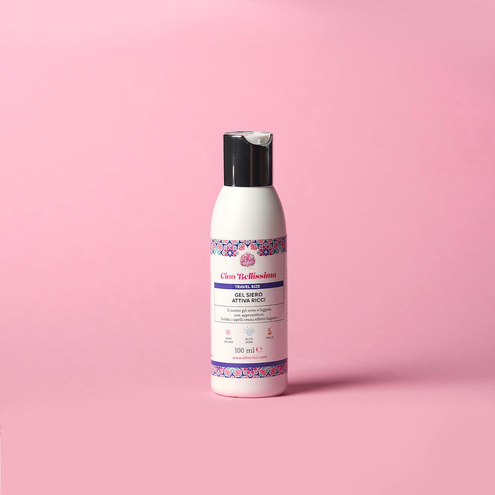 Flacone bianco con tappo nero. Scritta: Ciao Bellissima, Gel Siero Attiva Ricci. Sfondo rosa.