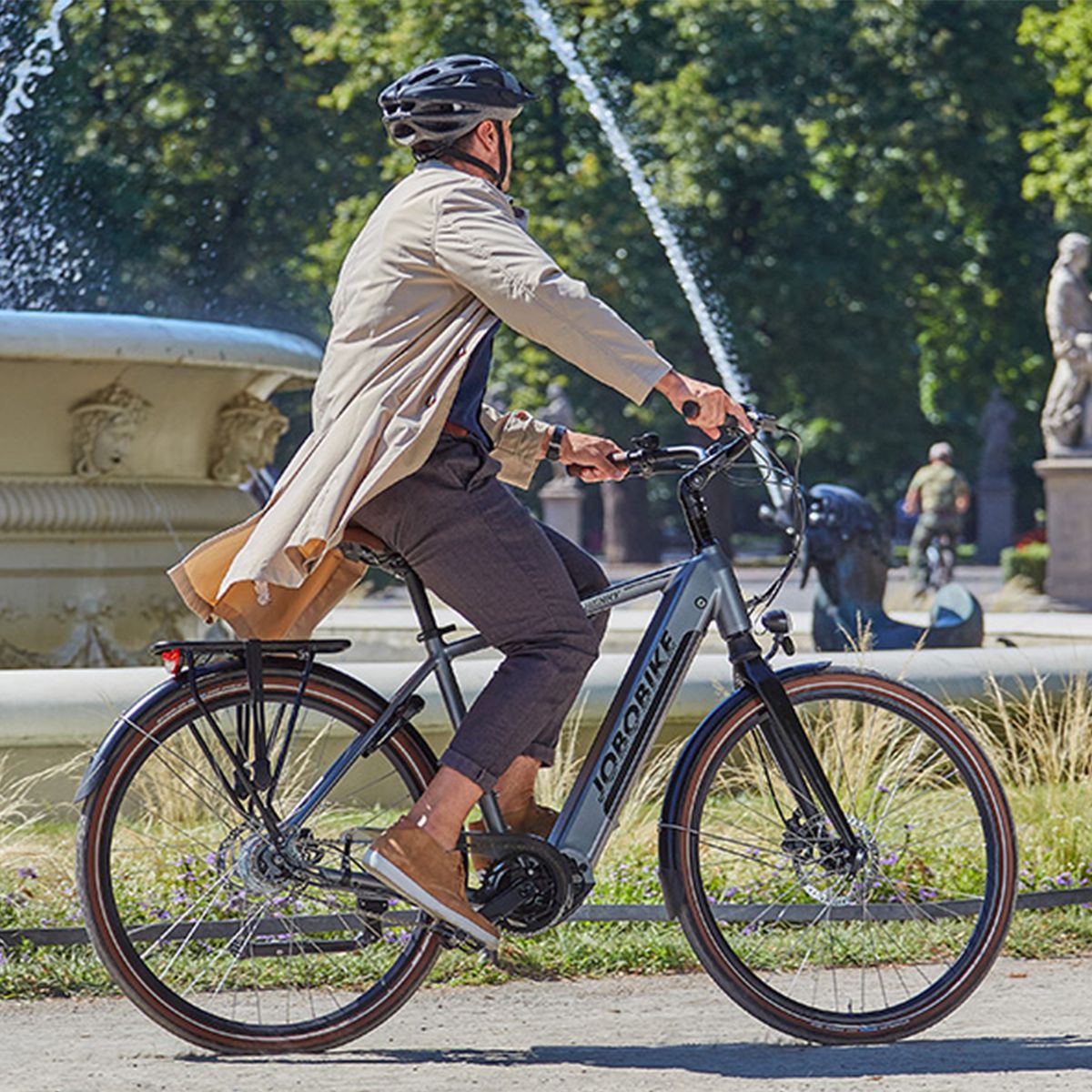 Persona che guida una e-bike grigia in un parco. Logo JOBOBIKE sul telaio.