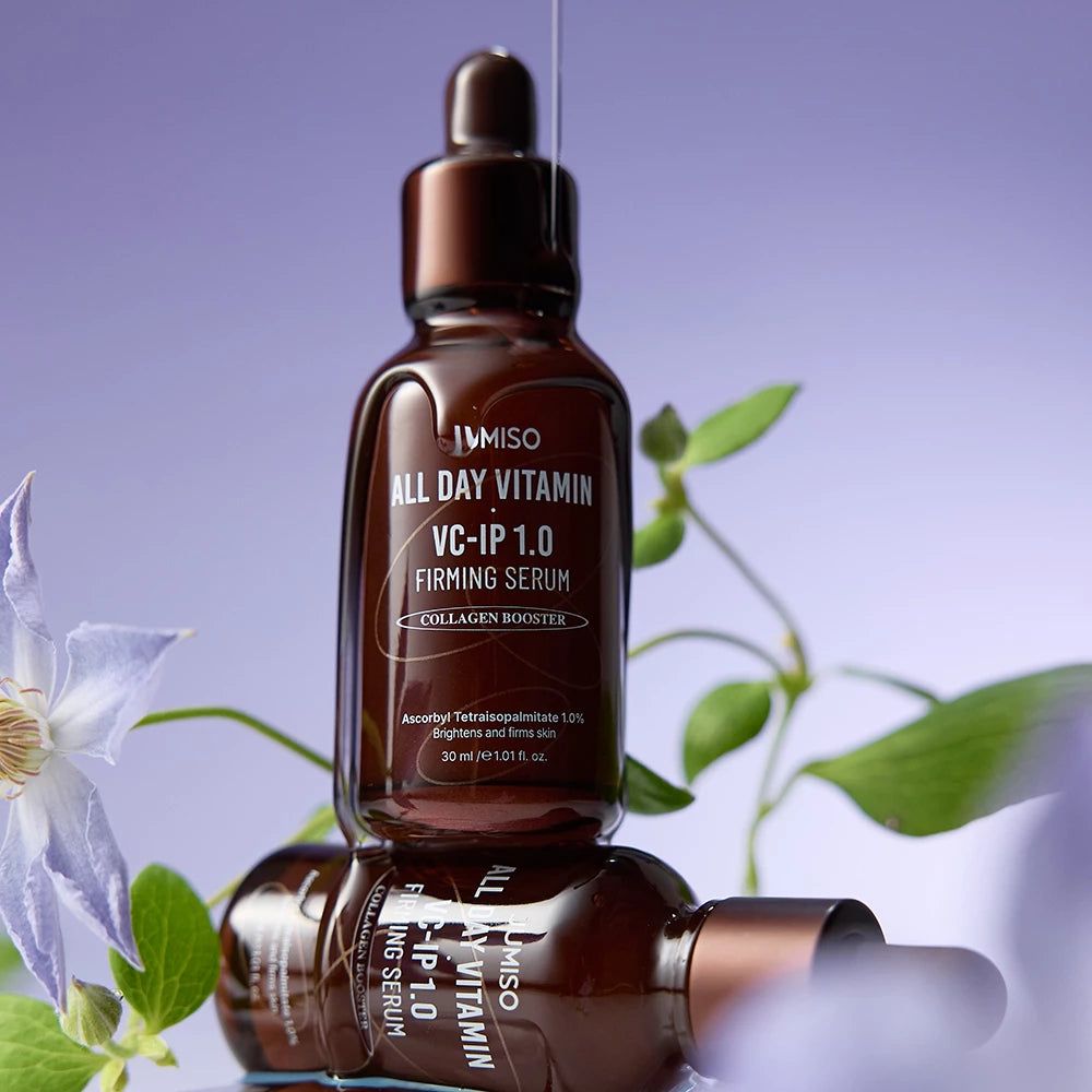 Due flaconi di siero rassodante JUMISO All Day Vitamin VC-IP 1.0 impilati con fiori.