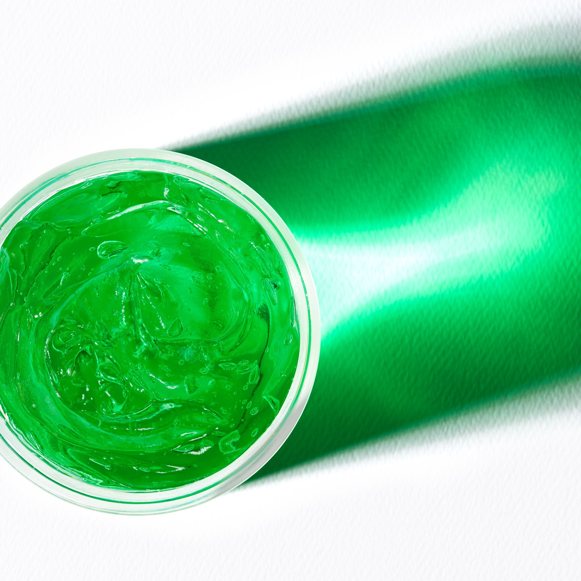 Vista dall'alto di gel verde in un contenitore trasparente. Un'ombra si proietta sulla superficie.