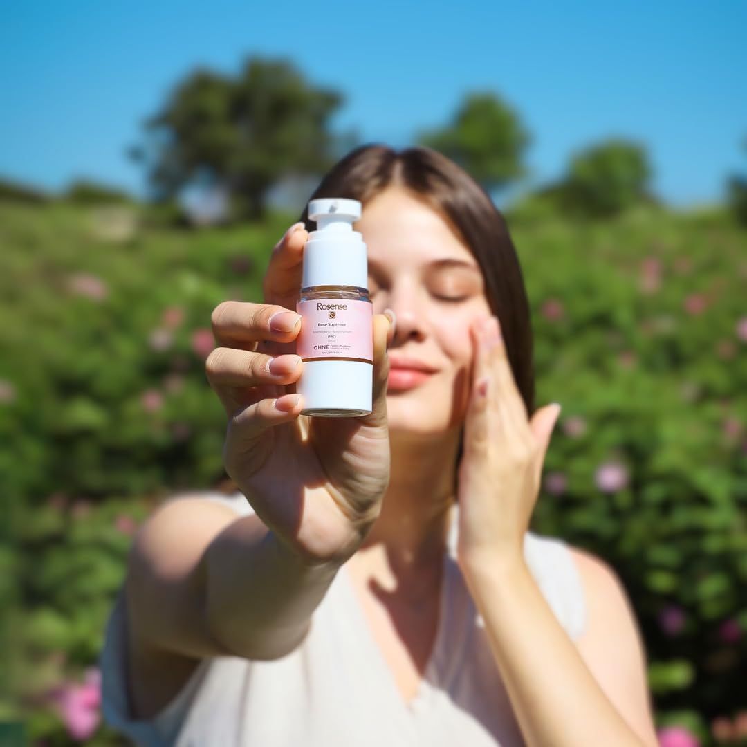 Donna tiene Rosense Supreme Augenserum. Dispenser bianco, etichetta rosa, testo. Donna tocca il viso. Sfondo: piante verdi.